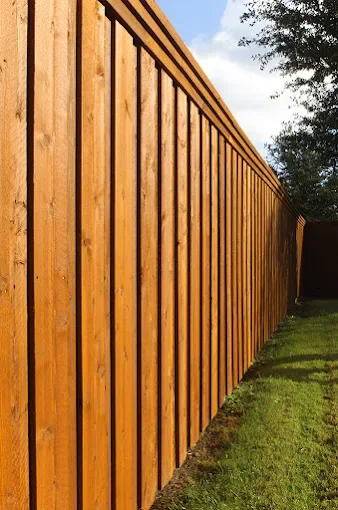 Wooden fence with vertical planks in a backyard, with grass and trees in the background.