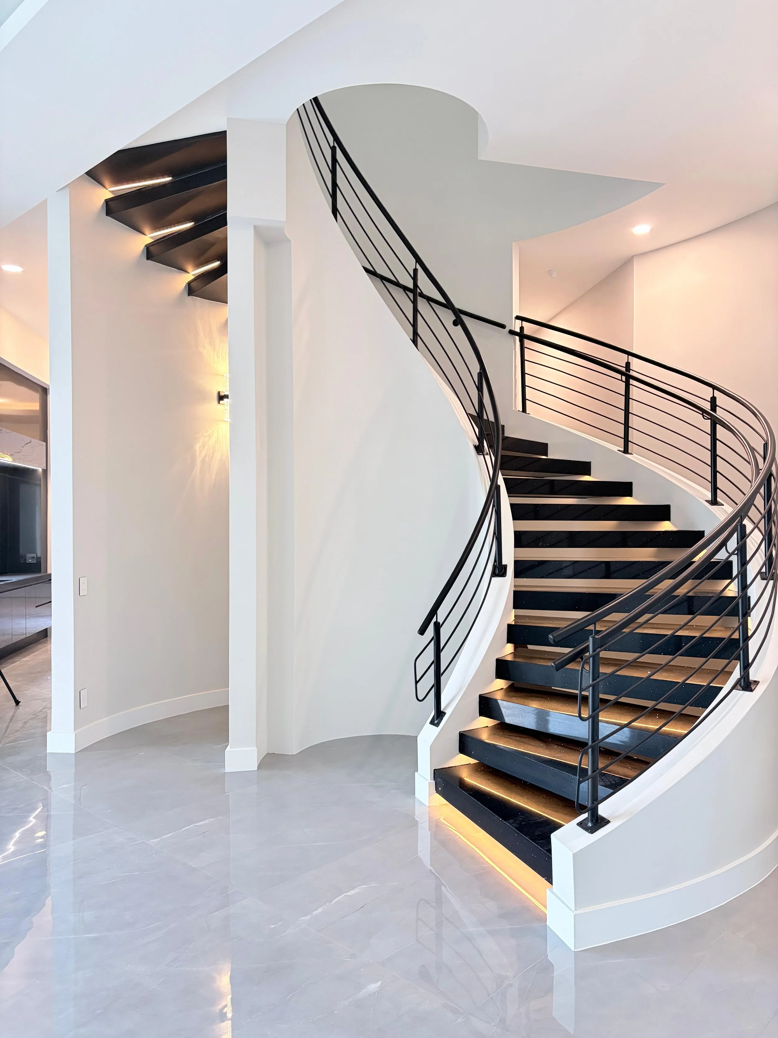 Modern curved staircase with black steps and black metal railing inside a bright, white interior