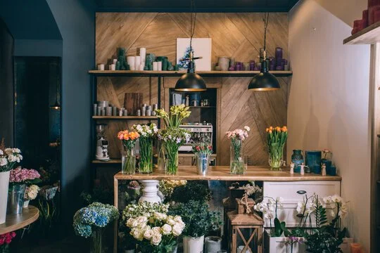 Flower shop display with various colorful flowers in vases and on shelves, wooden background, pendant lighting.
