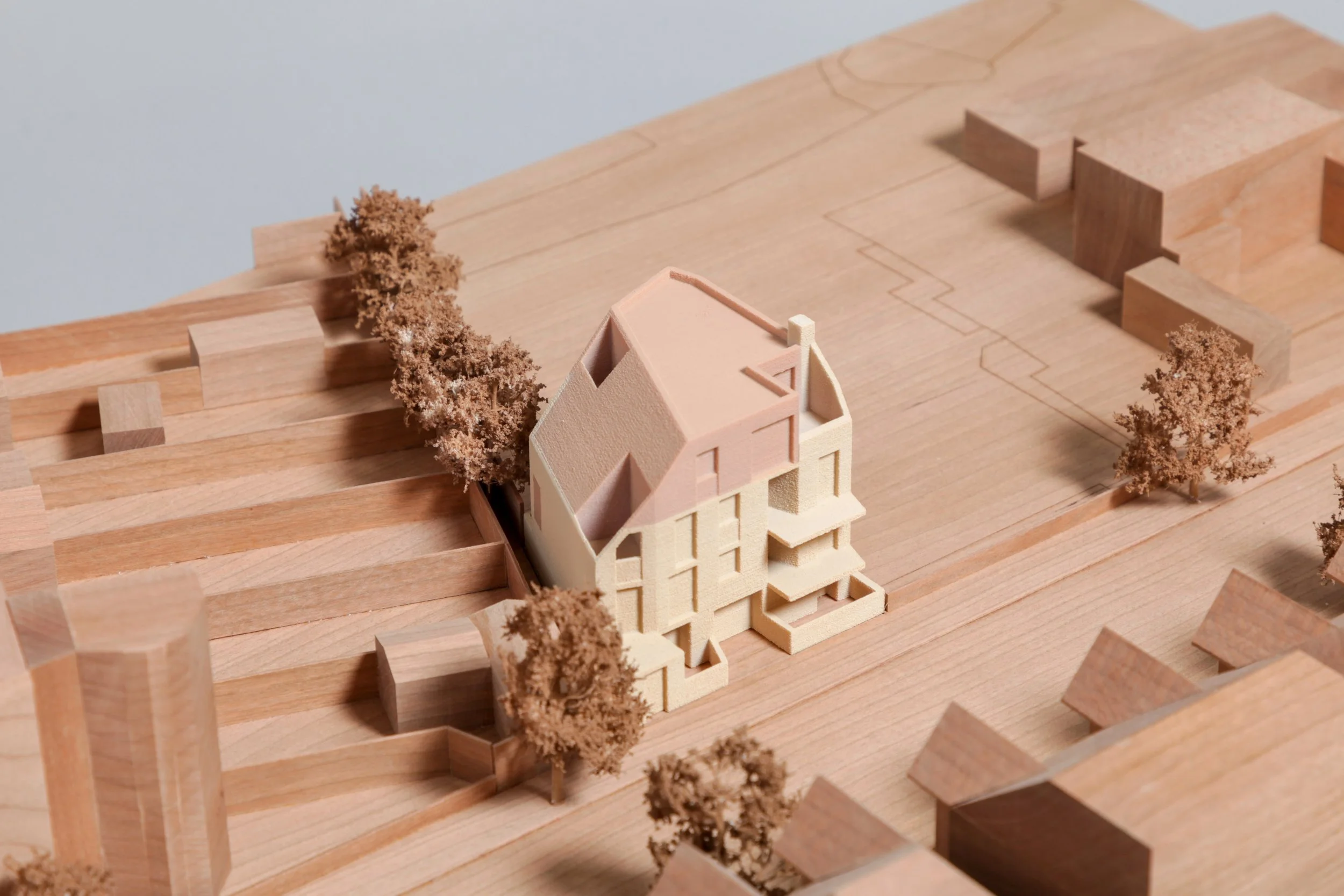 Architectural scale model of a multi-story house with trees and surrounding land on a wooden base.