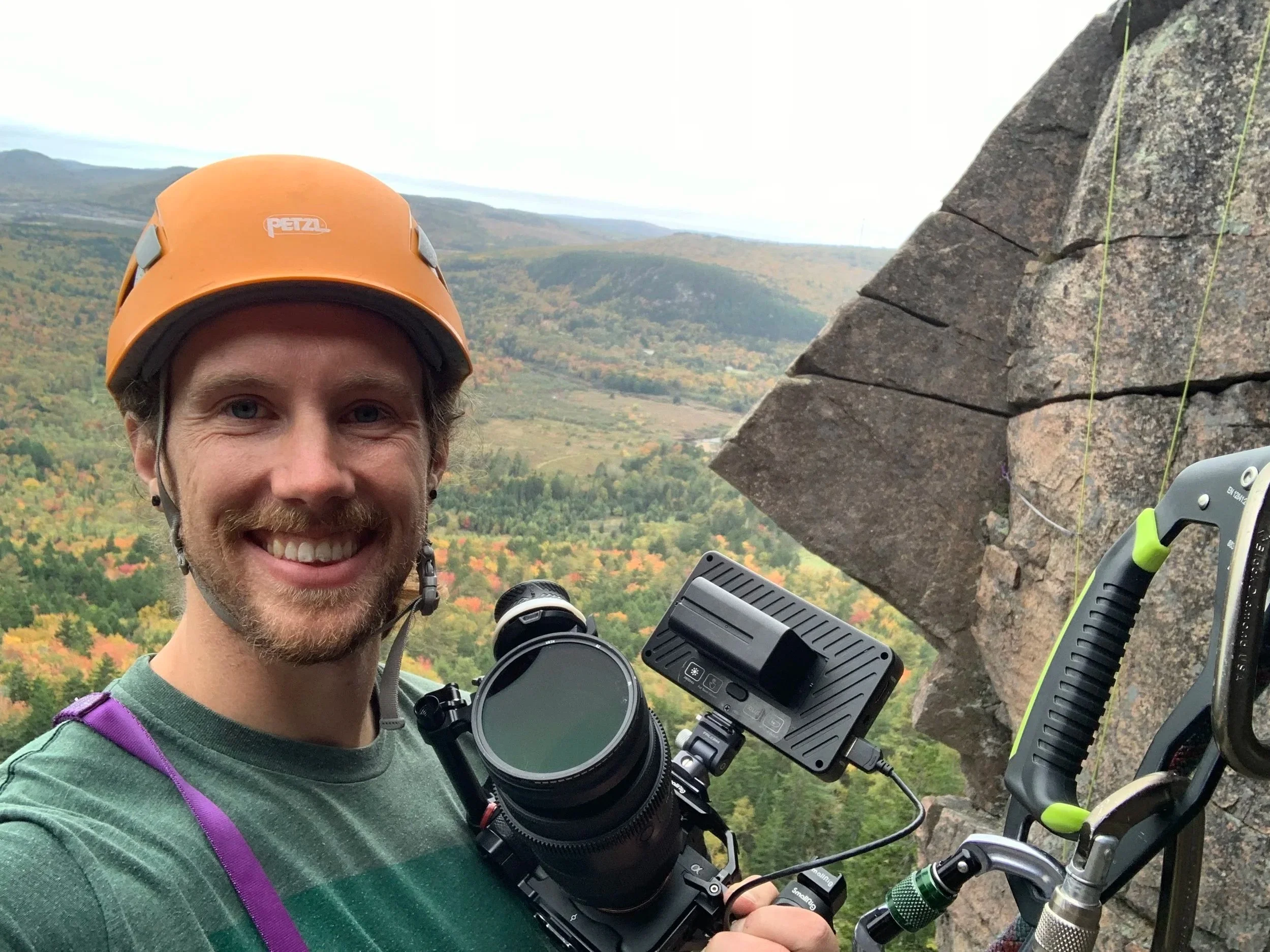 Photo of Tyler hanging off a mountain with a camera in hand