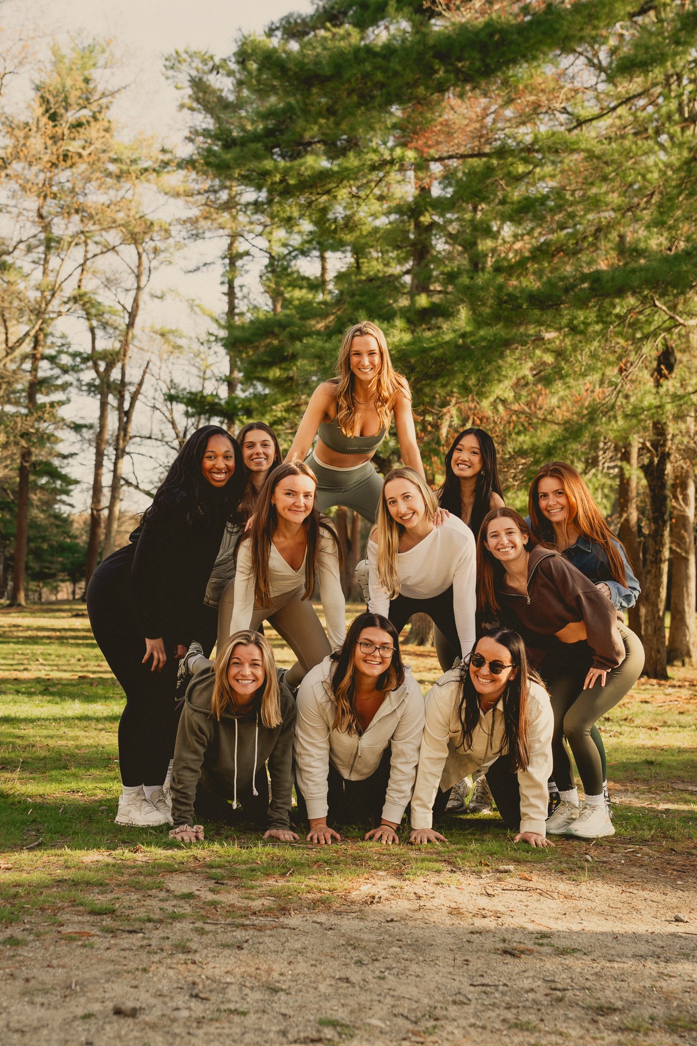 Group of women forming a human pyramid outdoors in a park with trees and grass.