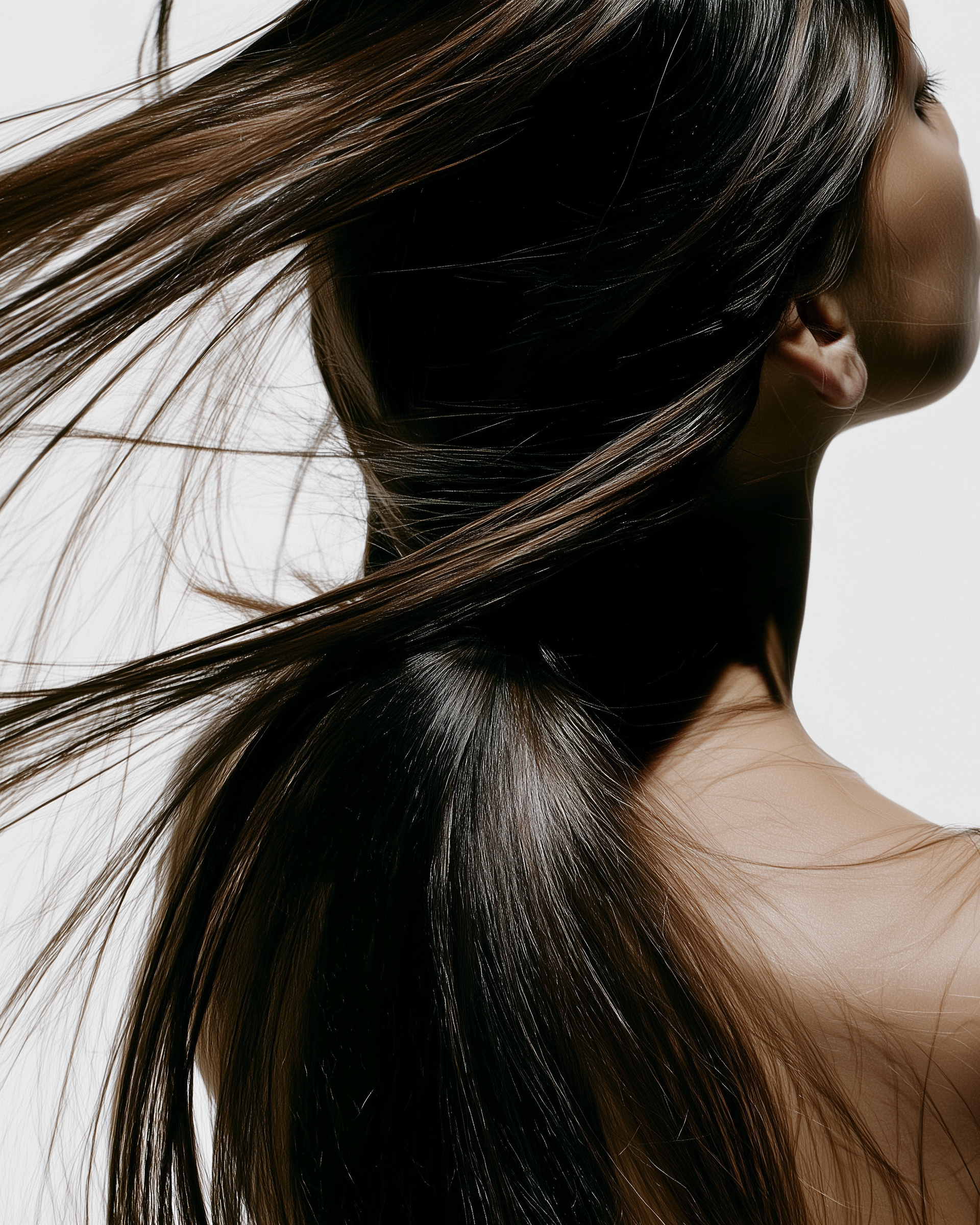 Close-up of a woman's glossy, dark brown hair flowing over her shoulder, with part of her face and neck visible against a plain background.