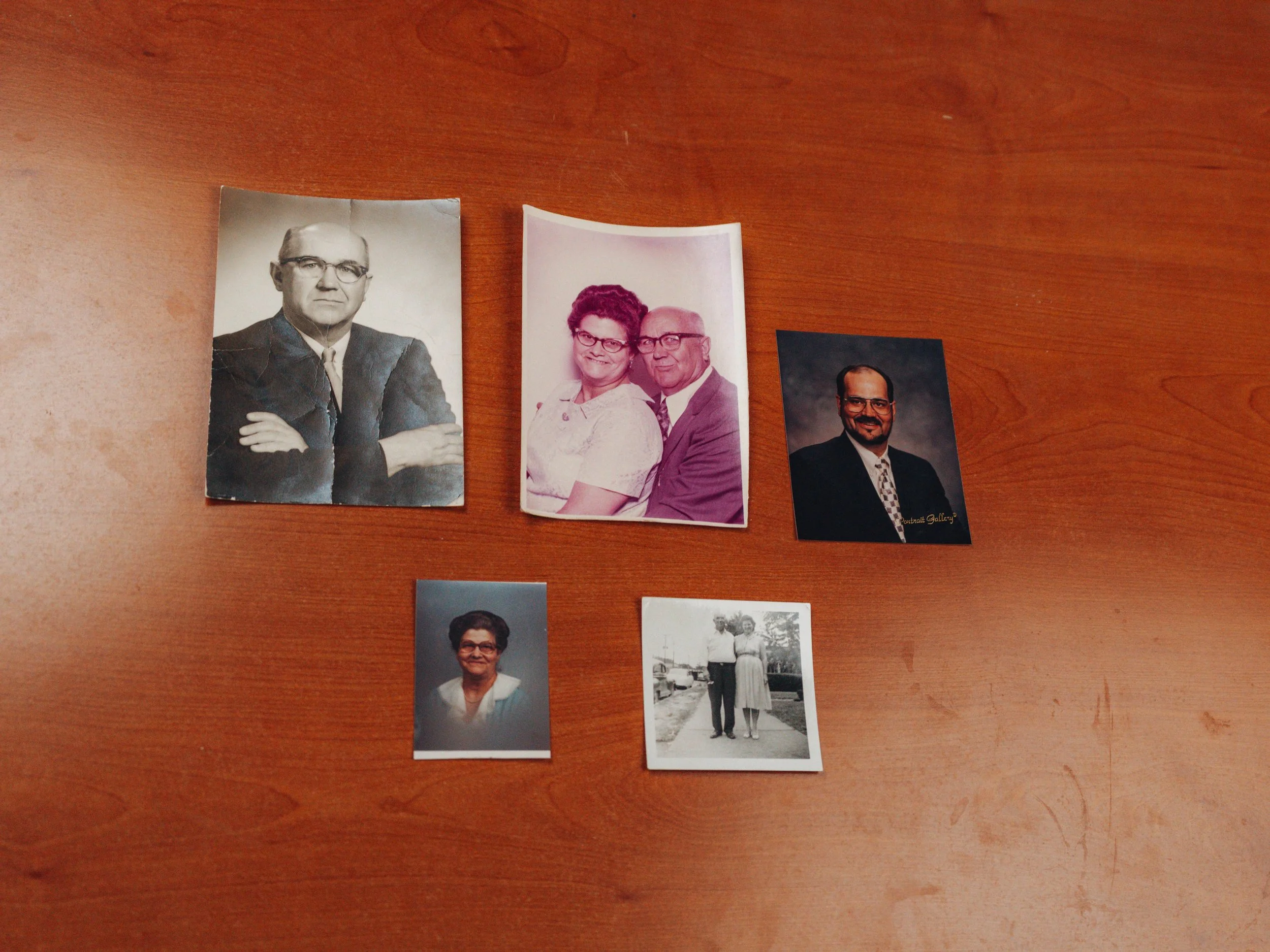 Five vintage photographs of people, including a black-and-white portrait of a man with glasses and crossed arms, a color photo of a woman and a man smiling, a headshot of a man with glasses, a black-and-white photo of a man and woman standing outdoors, and a headshot portrait of a woman with glasses.