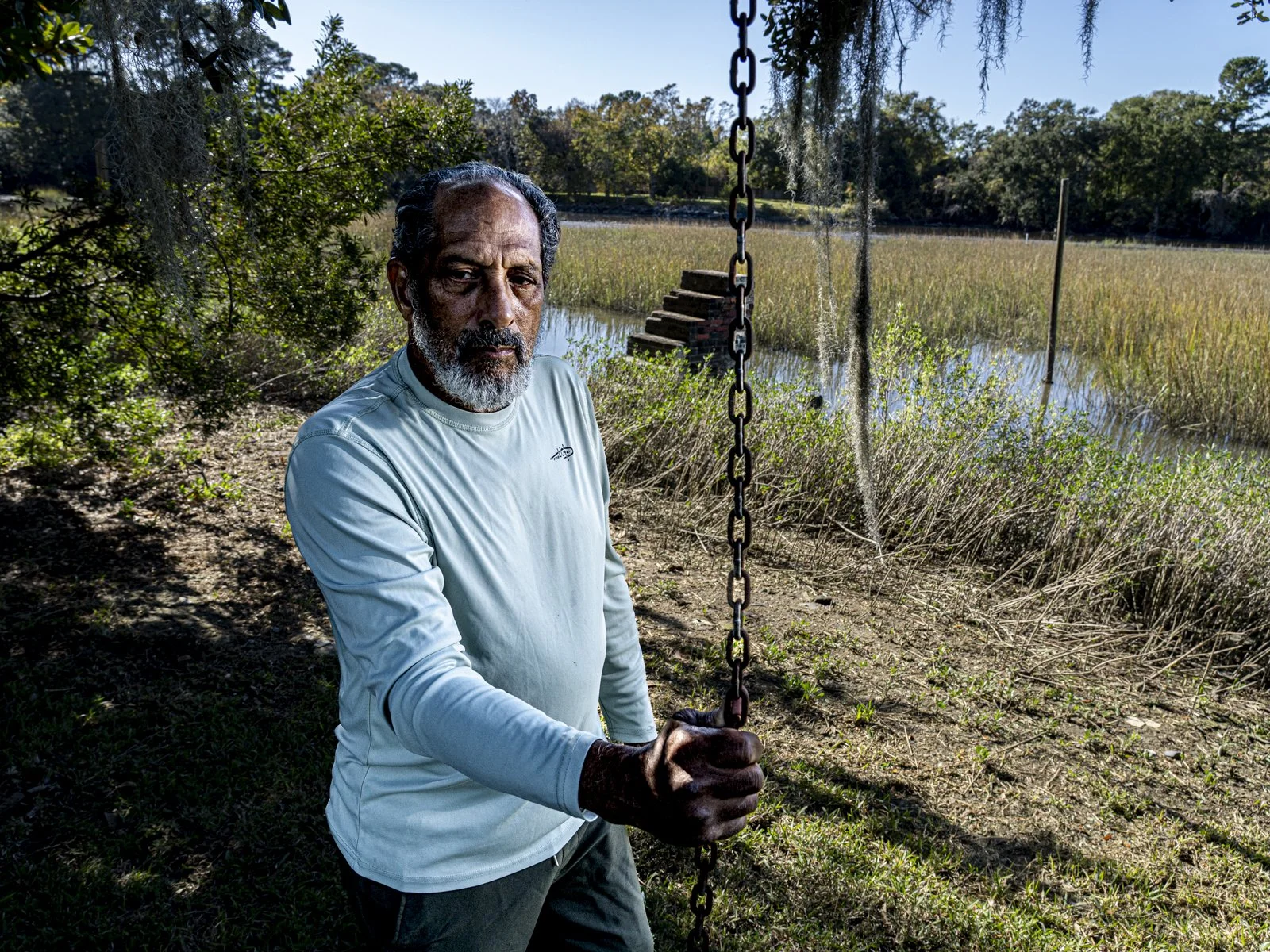 John Carr wearing a longsleeve shirt and holding a chain in front of the marsh, with a staircase in the background.