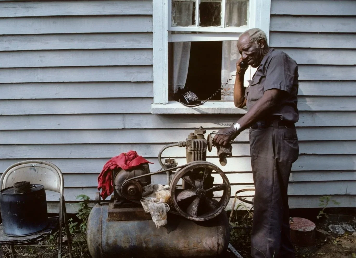 Historical image from 1987 of a man standing outside his home in front of a window with a landline phone.