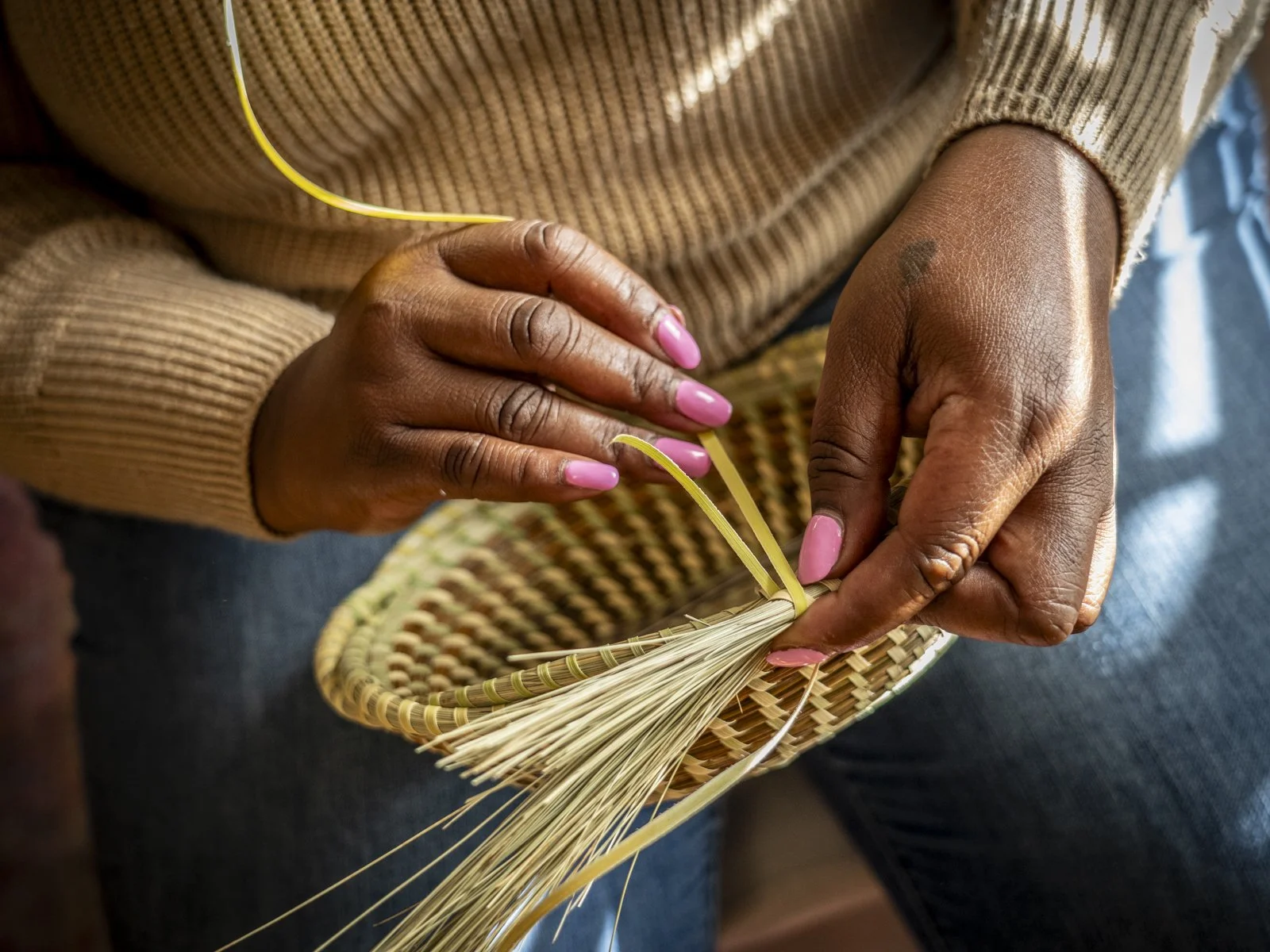 Andrea Cayetano Jefferson's hands working to sew a sweetgrass basket.