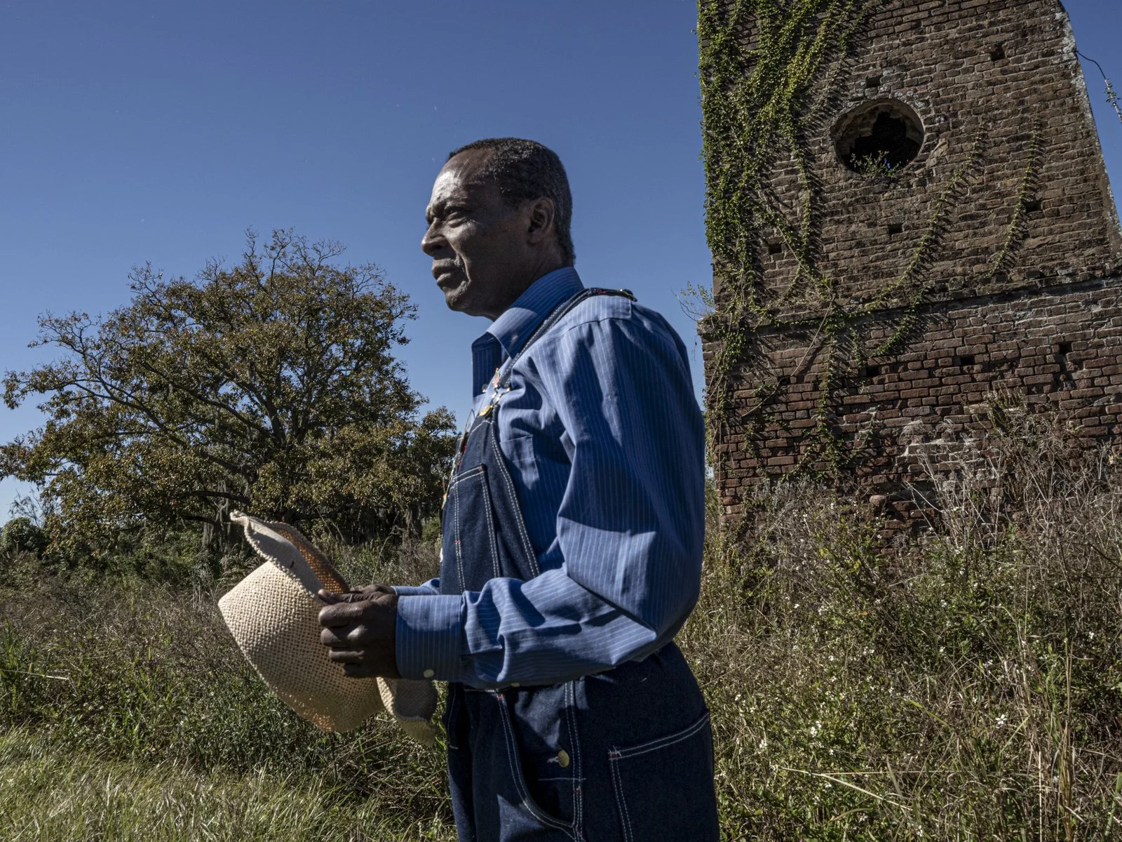 Award-winning image of Griffin Lotson outside, holding his hat, standing in front of the Enslaved People of Bulter Island monument.