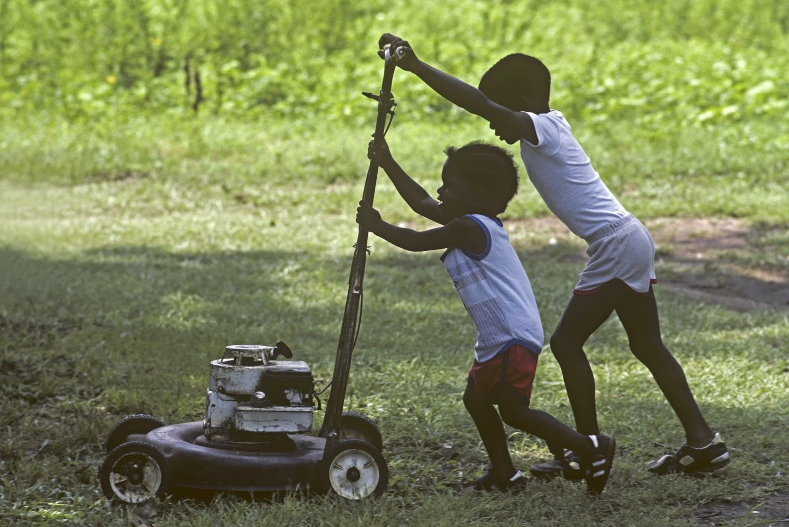 Historical image from 1987 of two young boys pushing a lawnmower.
