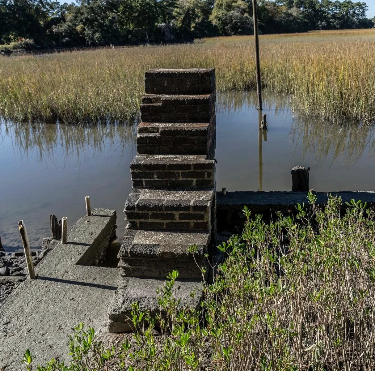 7-stair brick staircase leading up from a dock to nothing with marsh in the background.
