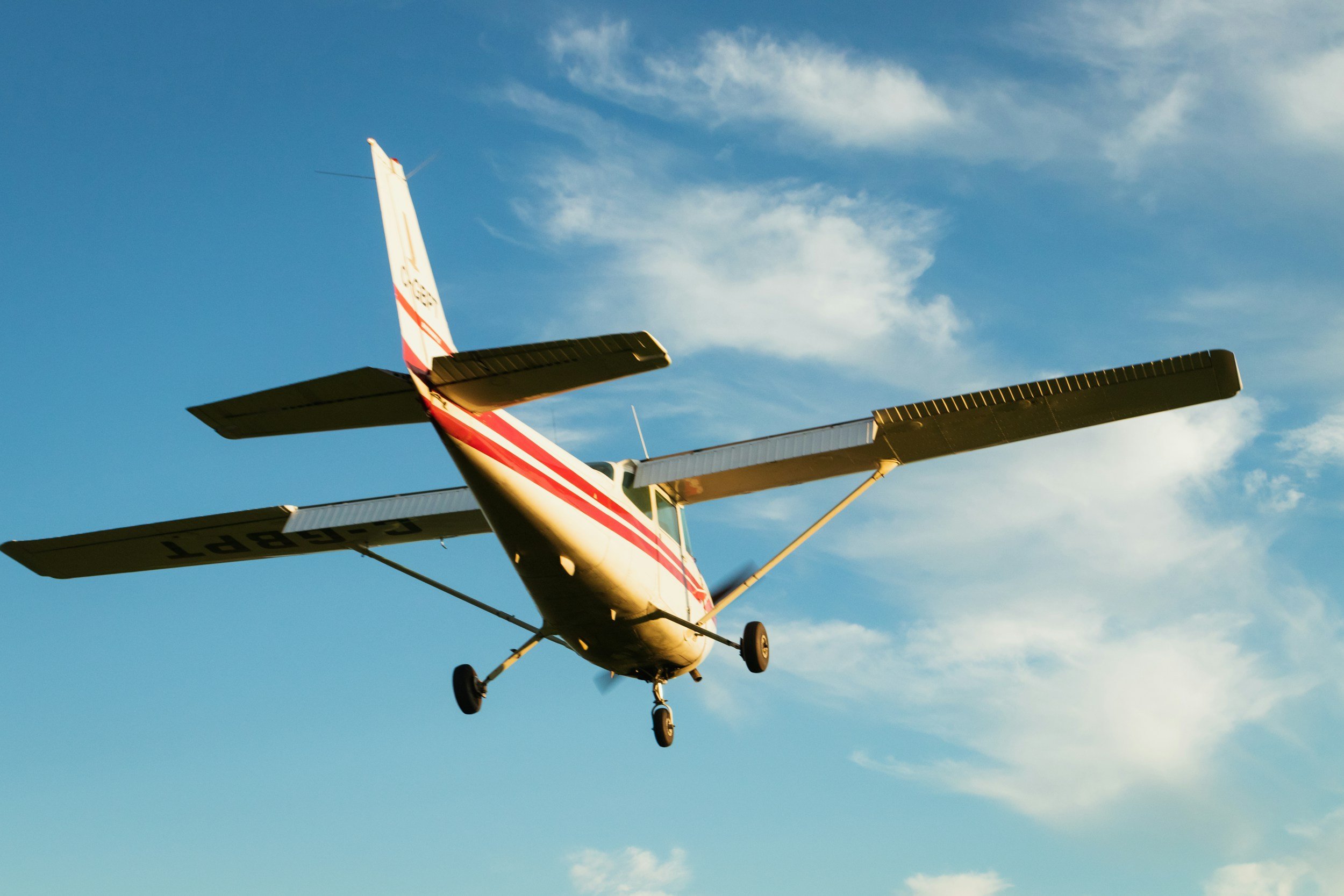 Small single-engine airplane flying in a clear blue sky with a few wispy clouds flight training takeoff.
