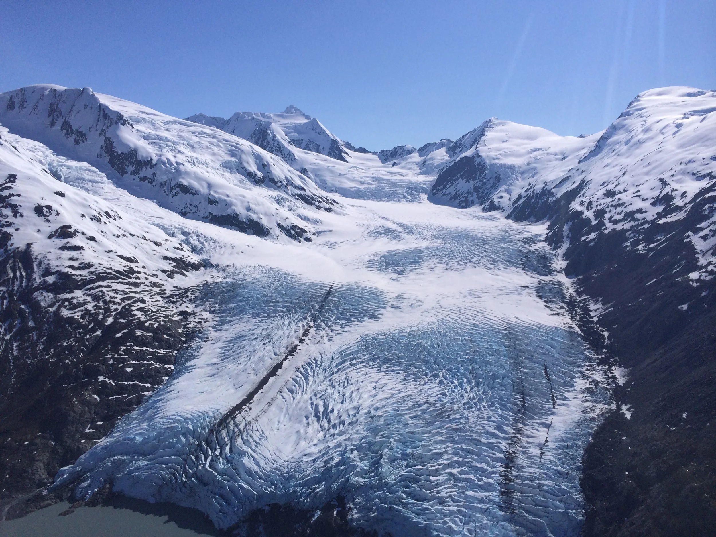 Snowy mountain range with glaciers and a clear blue sky.