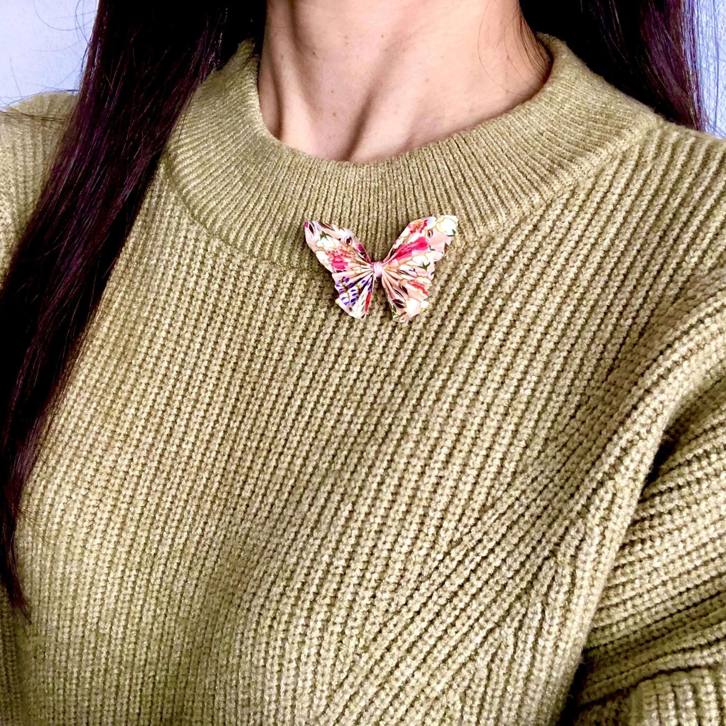 Un col roulé beige avec une broche en papillon en papier japonais fixé à l'avant.