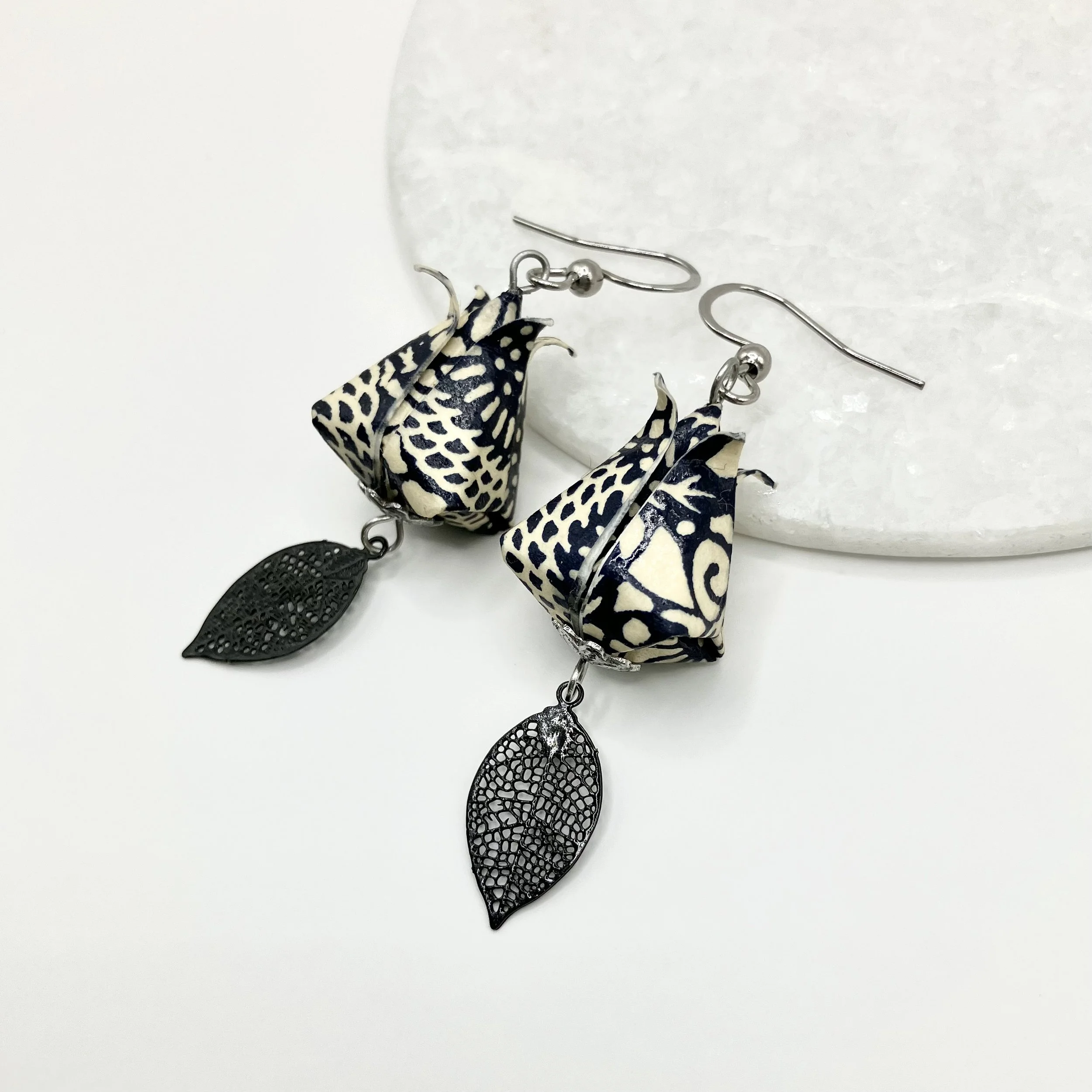 Boucles d'oreilles en forme de tulipe avec des feuilles en métal noir perforé et en papier japonais avec motif floral noir et blanc.