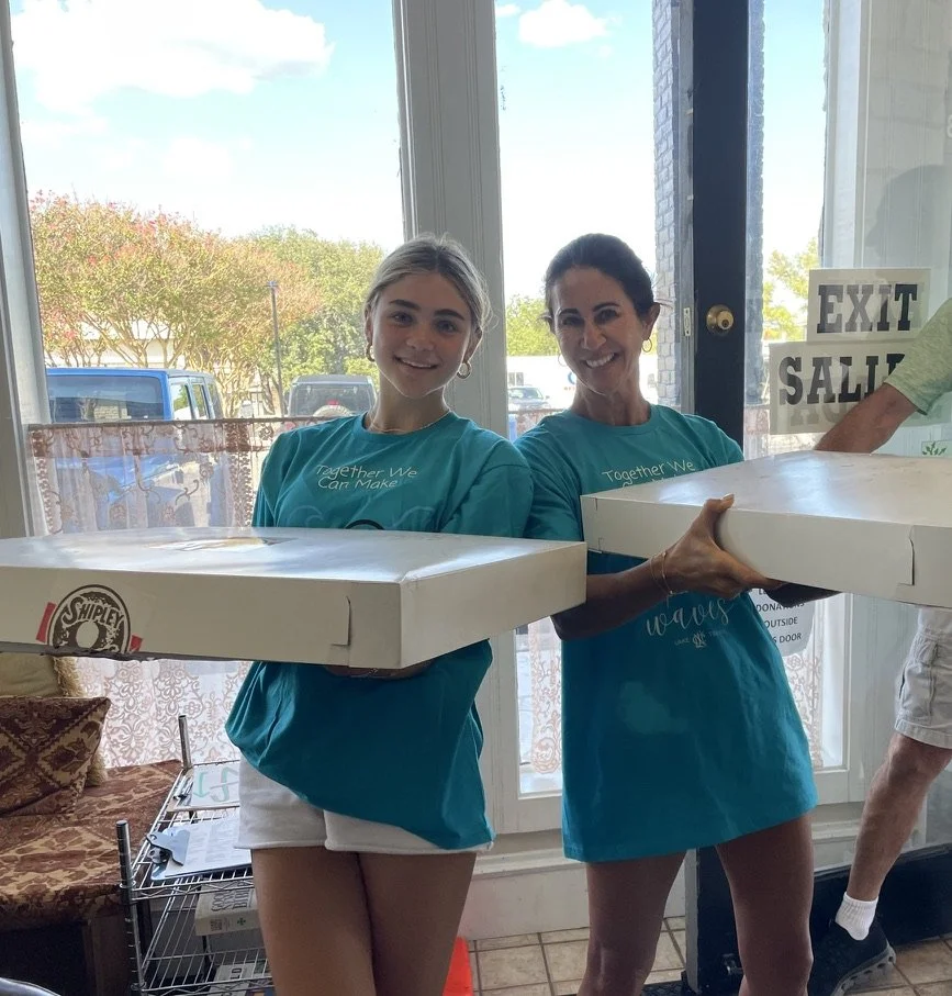 Two smiling women holding pizza boxes inside restaurant near exit door with outdoor view.