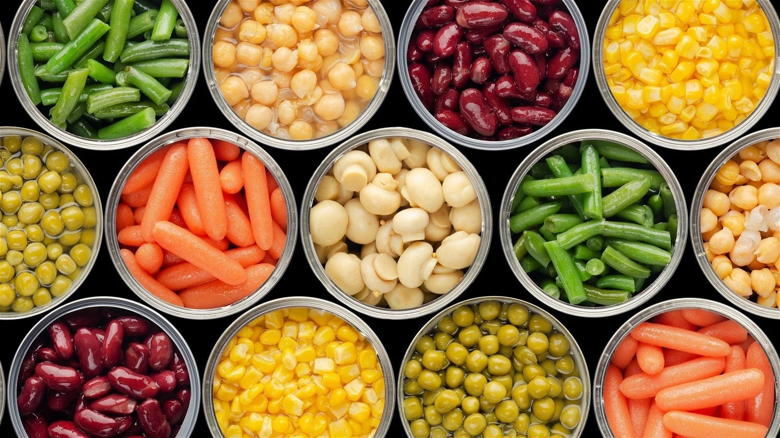 Assorted canned vegetables, including green beans, chickpeas, kidney beans, corn, peas, carrots, and wax beans, arranged in circular containers on a black background.