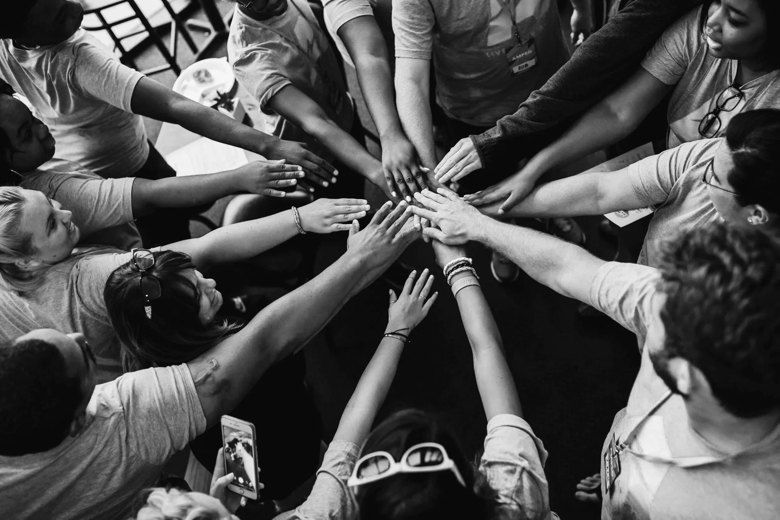 Group of diverse people with their hands stacked together in the center, symbolizing unity and teamwork.