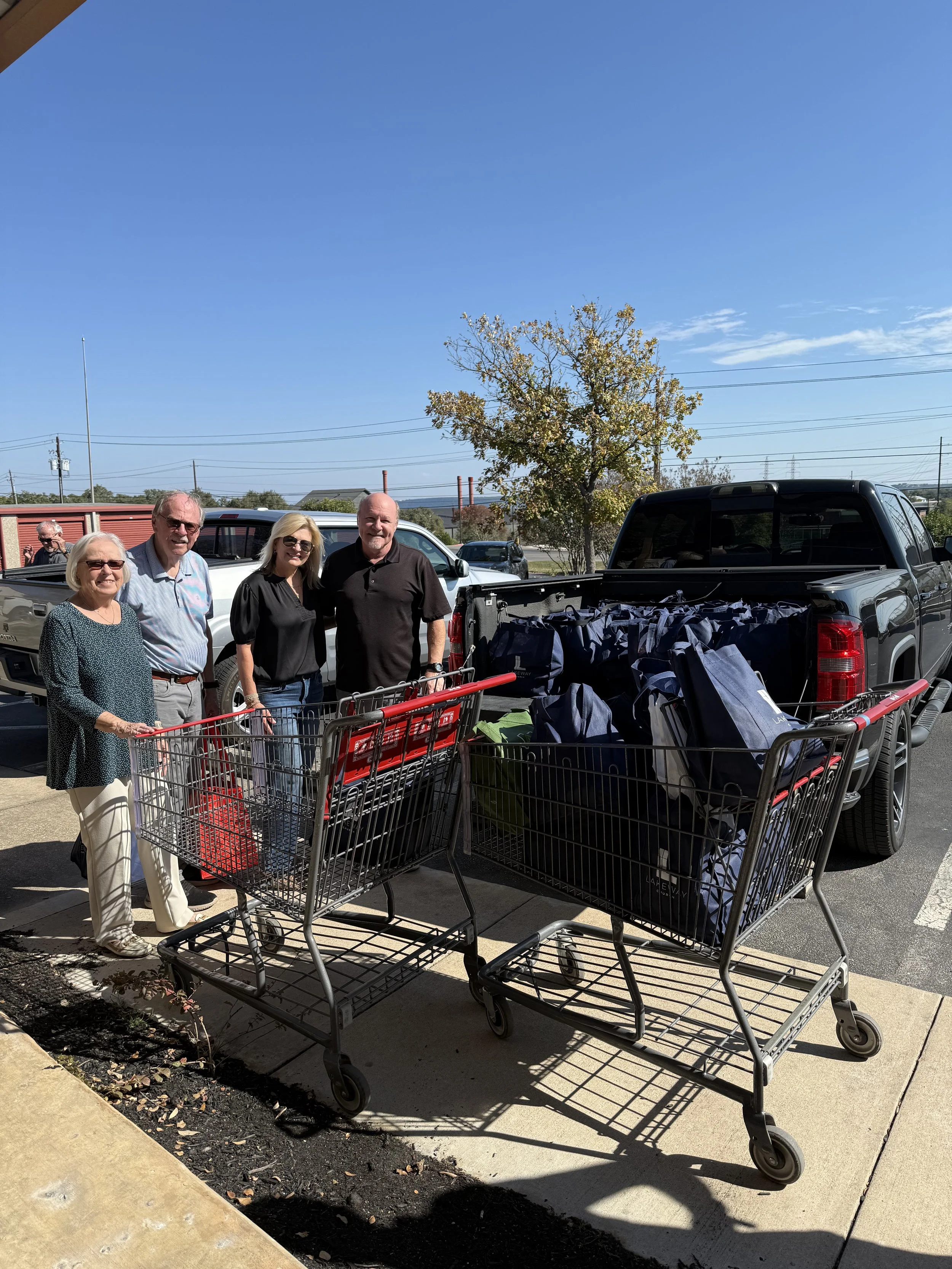 Four people standing behind shopping carts filled with bags and boxes outside on a sunny day.