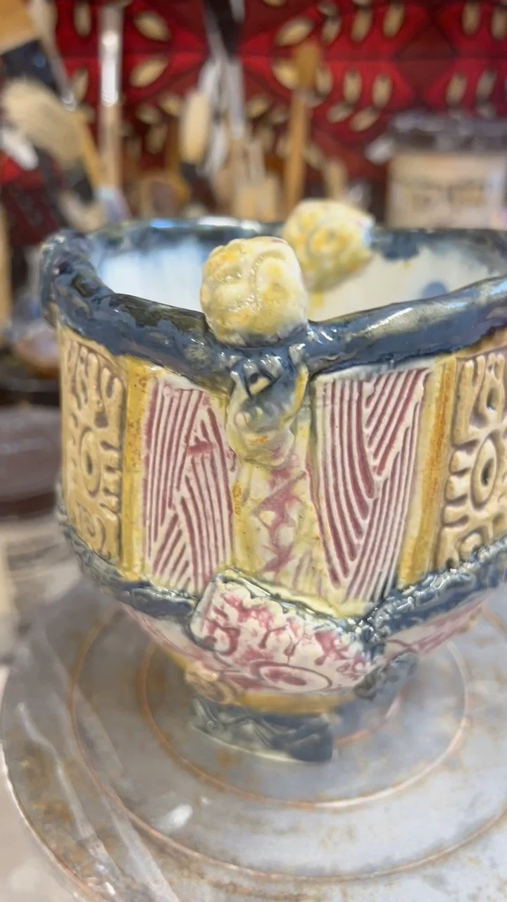 Close view of Story Bowl 1 showing colorful carved panels, textured clay, and blue glazed rim.