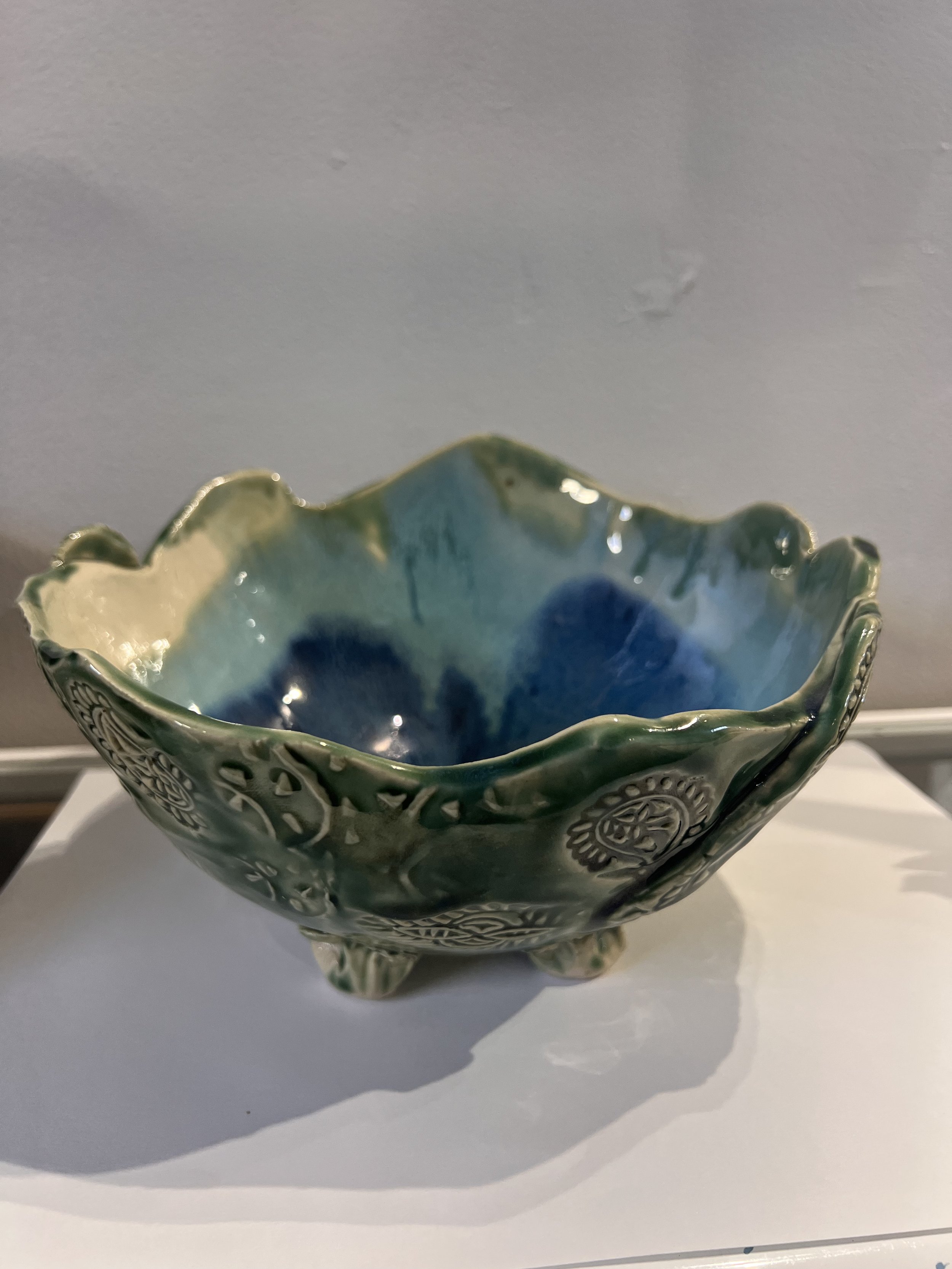 Side view of blue-green glazed stoneware bowl with raised feet, textured outer surface, and scalloped rim.