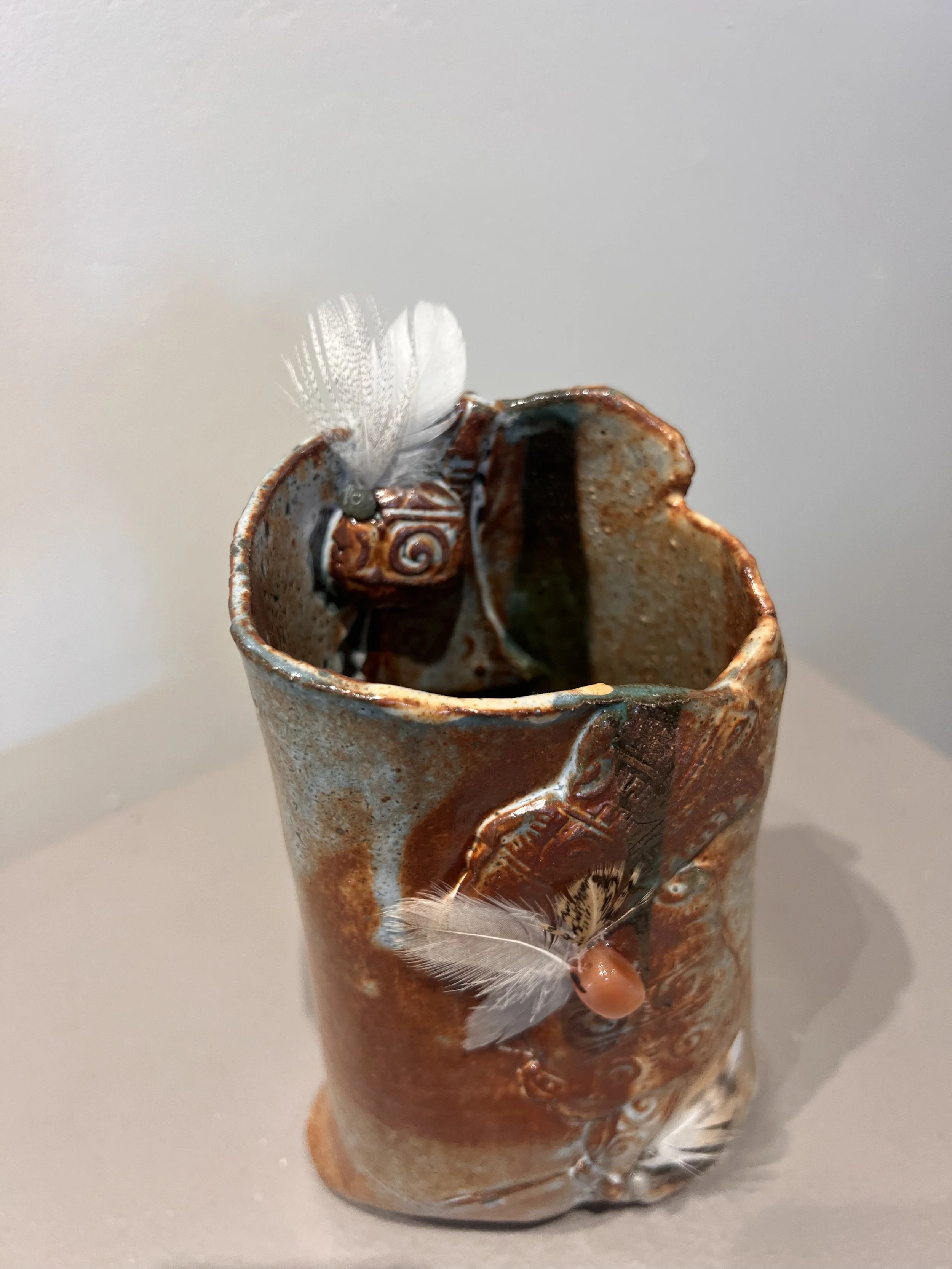 Earthy stoneware vessel with feathers, beads, and textured glaze suggesting bird spirit and fire.