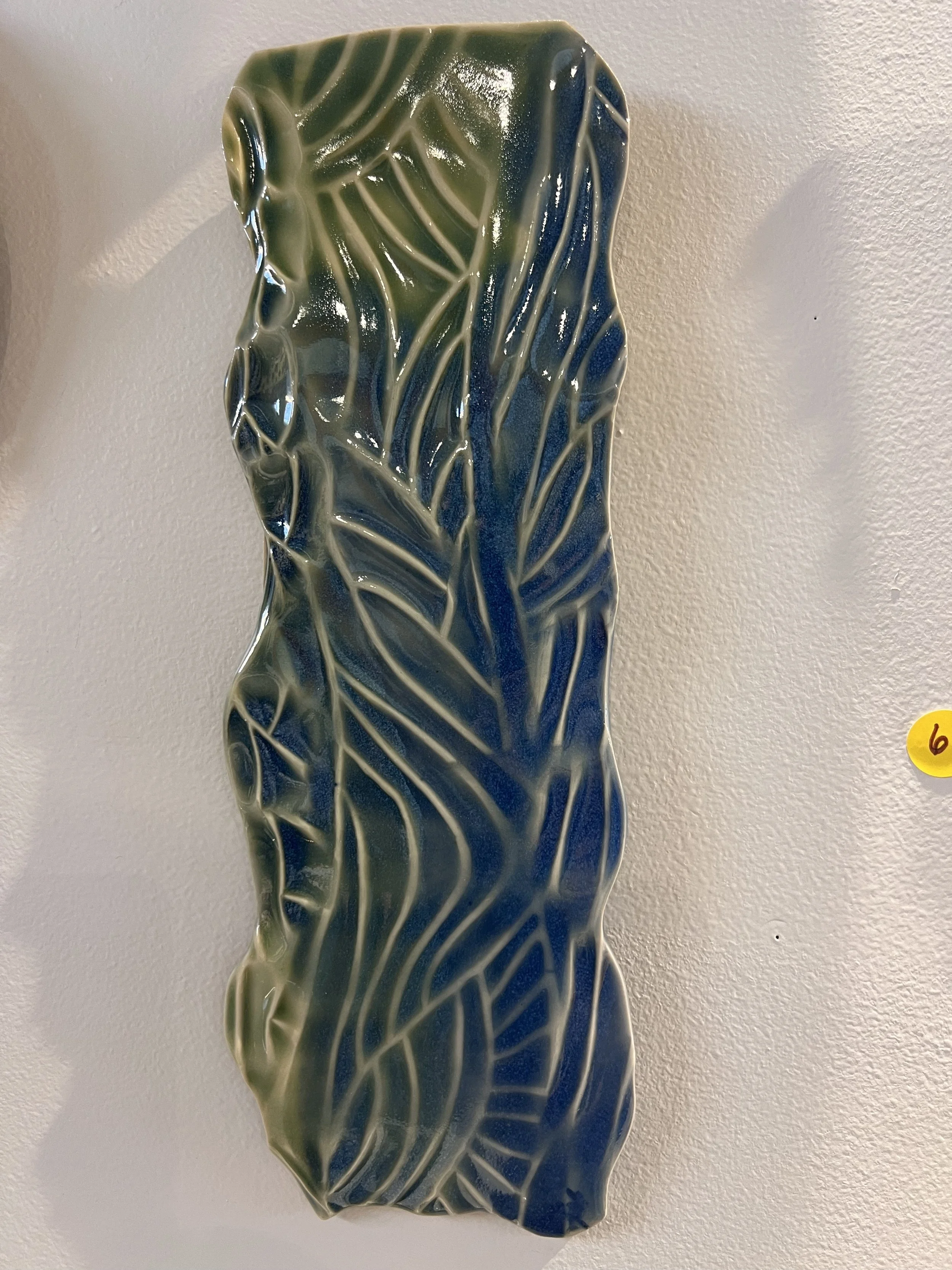 Tall textured stoneware wall piece with blue-green glaze and flowing wave-like carved patterns.
