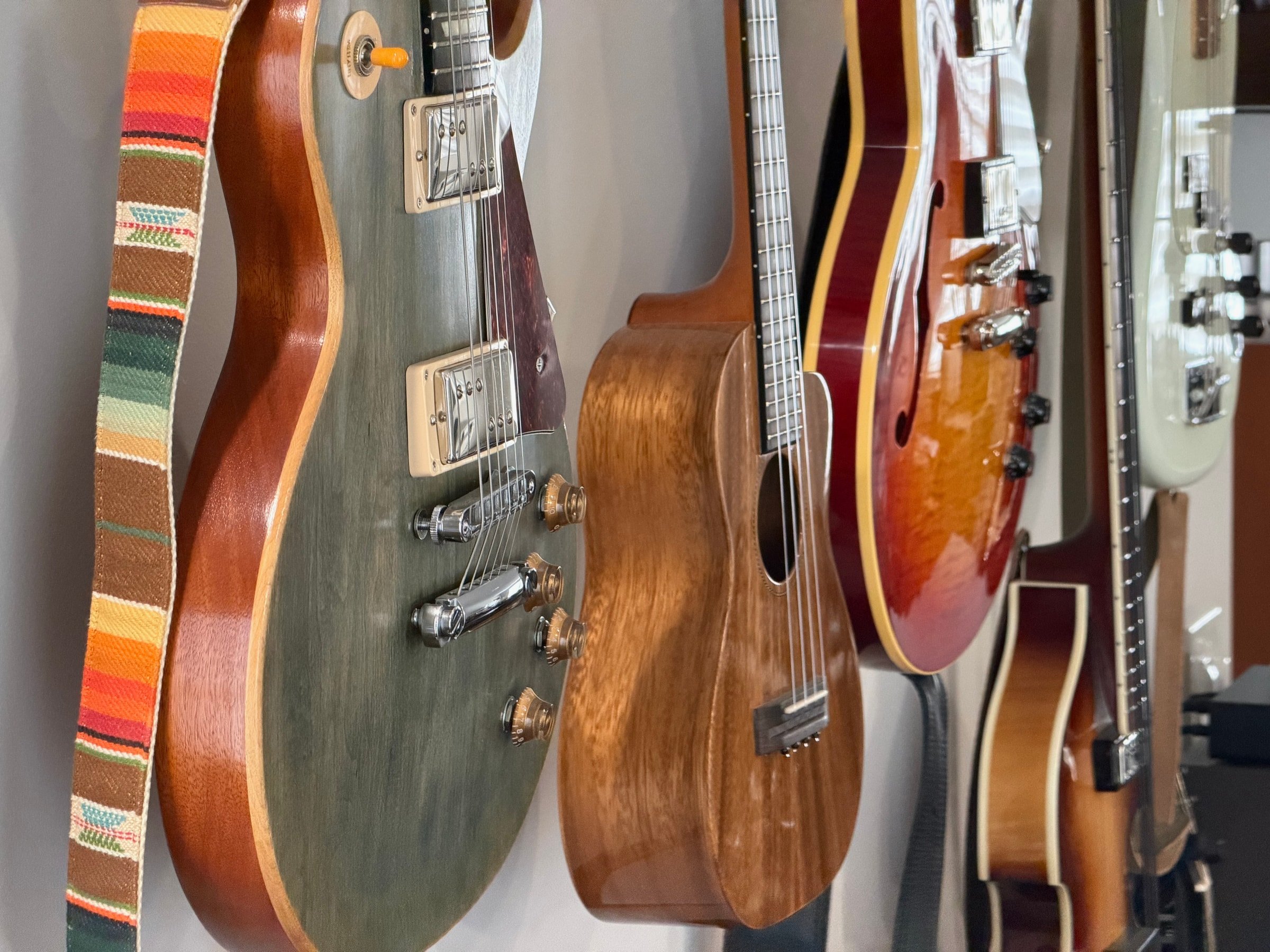 Electric guitars, a wooden ukulele, and bass guitars hanging on the Audio Sails studio wall.