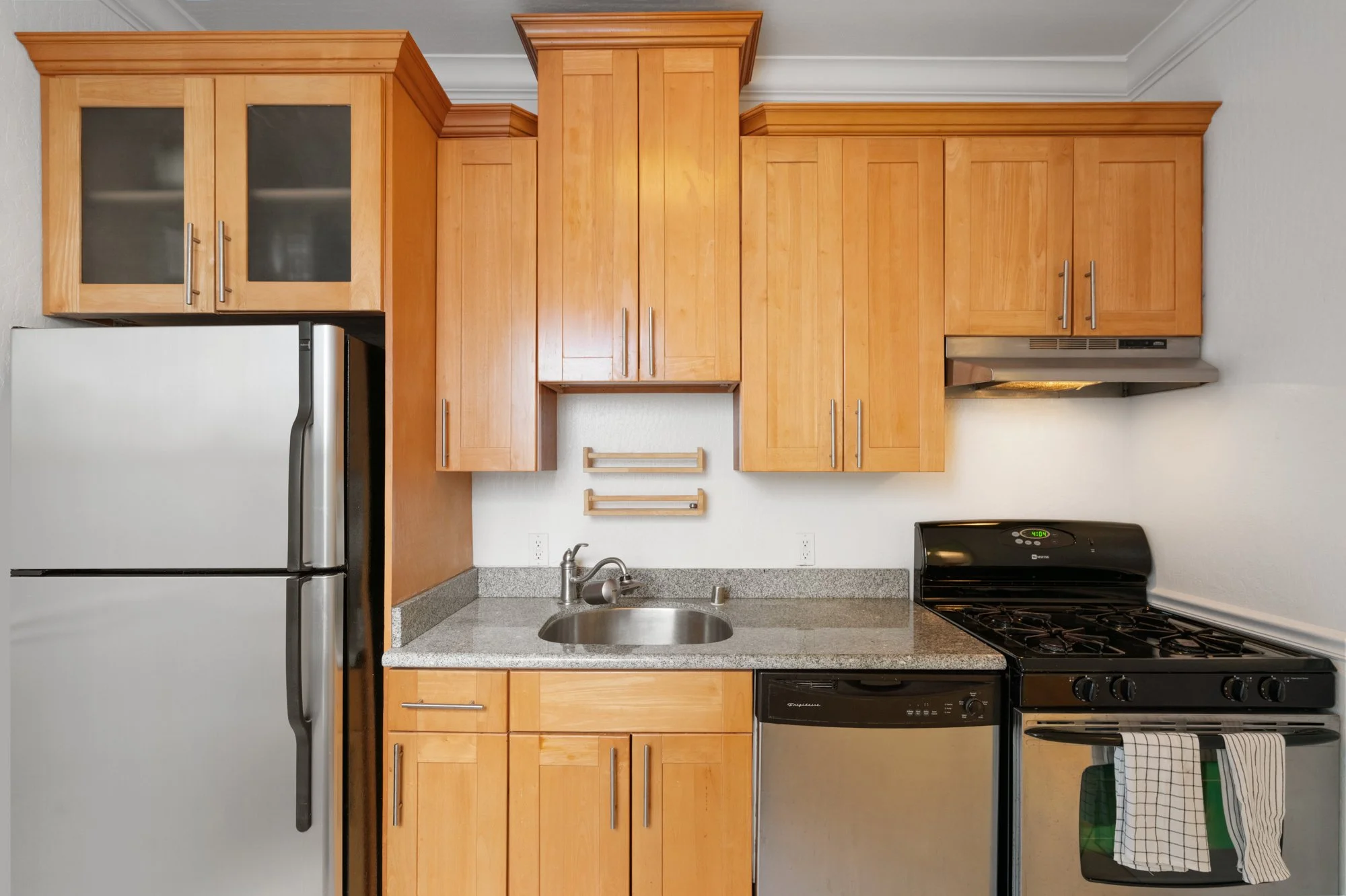 Kitchen with light wood cabinets, a stainless steel refrigerator, a small stainless steel sink, a gray granite countertop, a black gas stove with an oven, and a dishwasher beneath the counter.