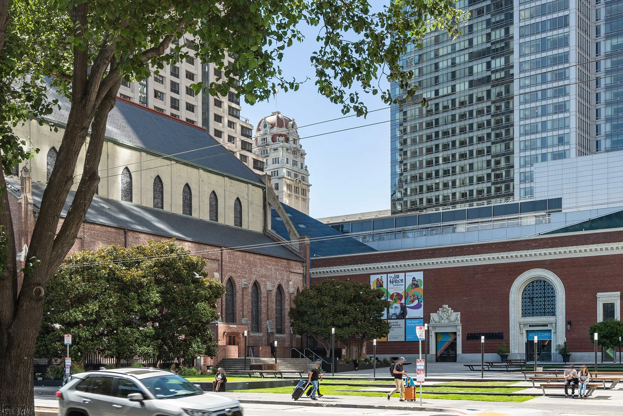 Street view showing a historic church building with brick and stone architecture, surrounded by trees and modern skyscrapers in downtown.