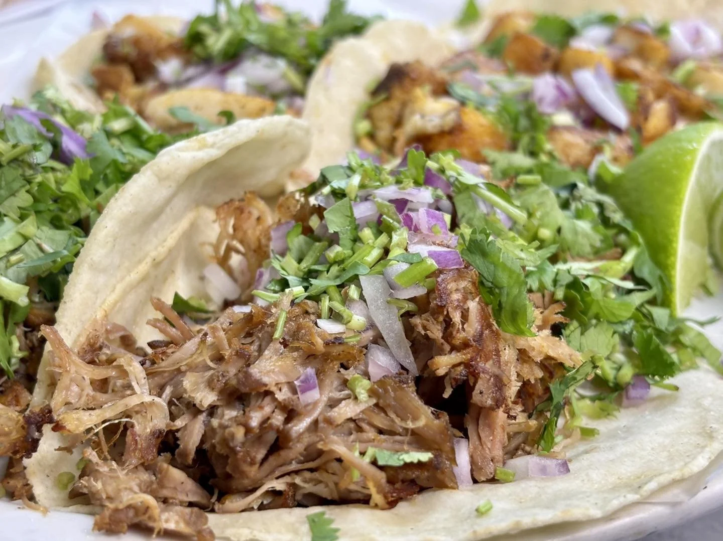 Close-up of shredded meat tacos garnished with chopped onions, cilantro, and a lime wedge.