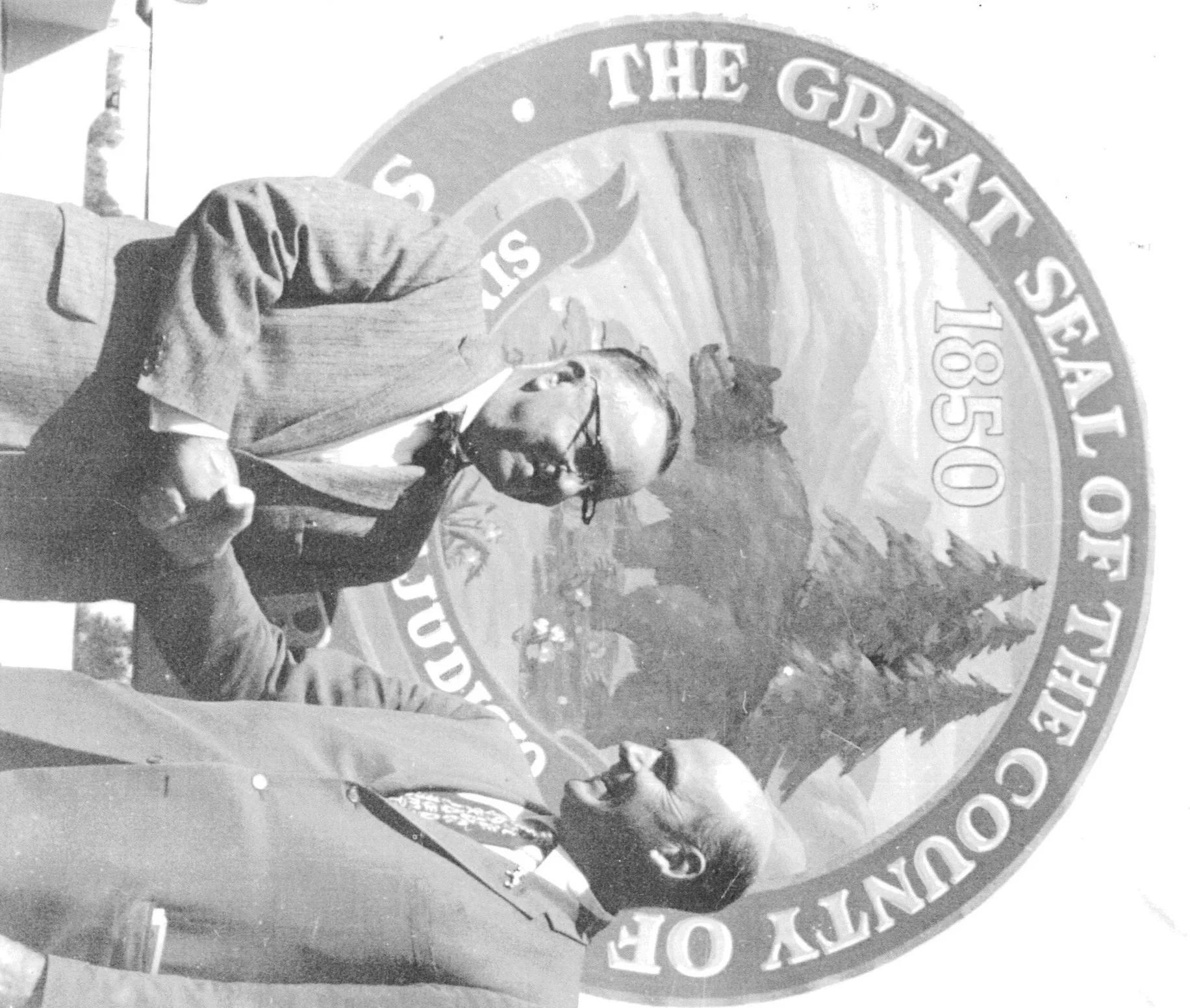 John Francis Kane shaking hands with a business man in front of a Santa Cruz County State Seal