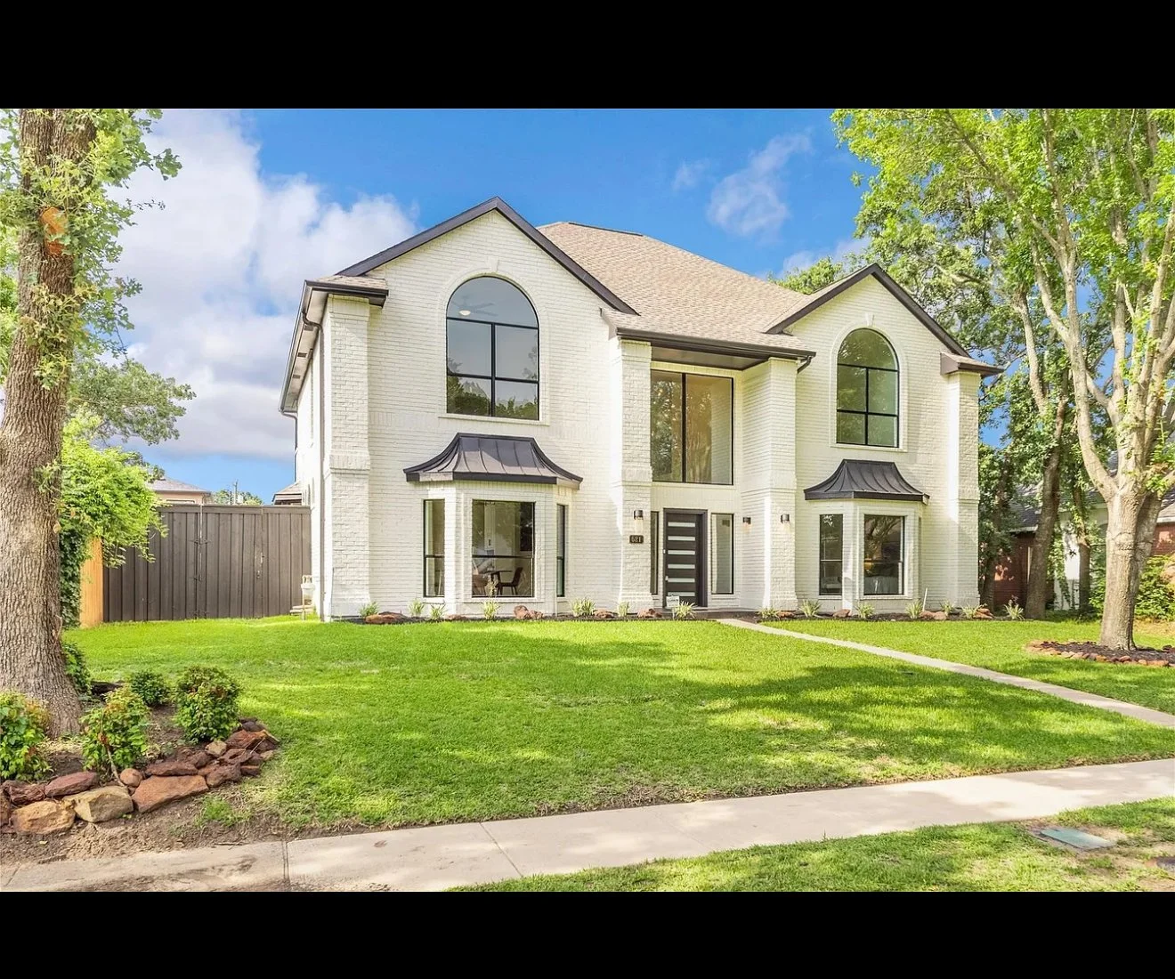 Front view of a two-story white brick house with black accents, large arched windows, and a well-maintained lawn with trees and a sidewalk luxury sold property