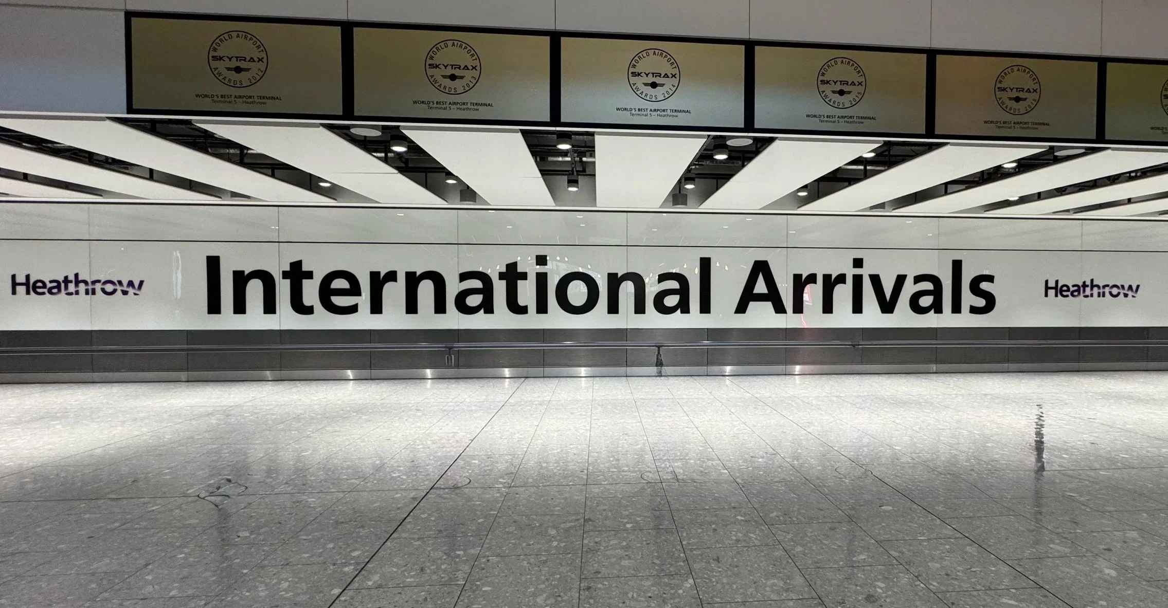 Sign at Heathrow Airport showing 'International Arrivals' in large black letters and Heathrow logo repeated on either side.