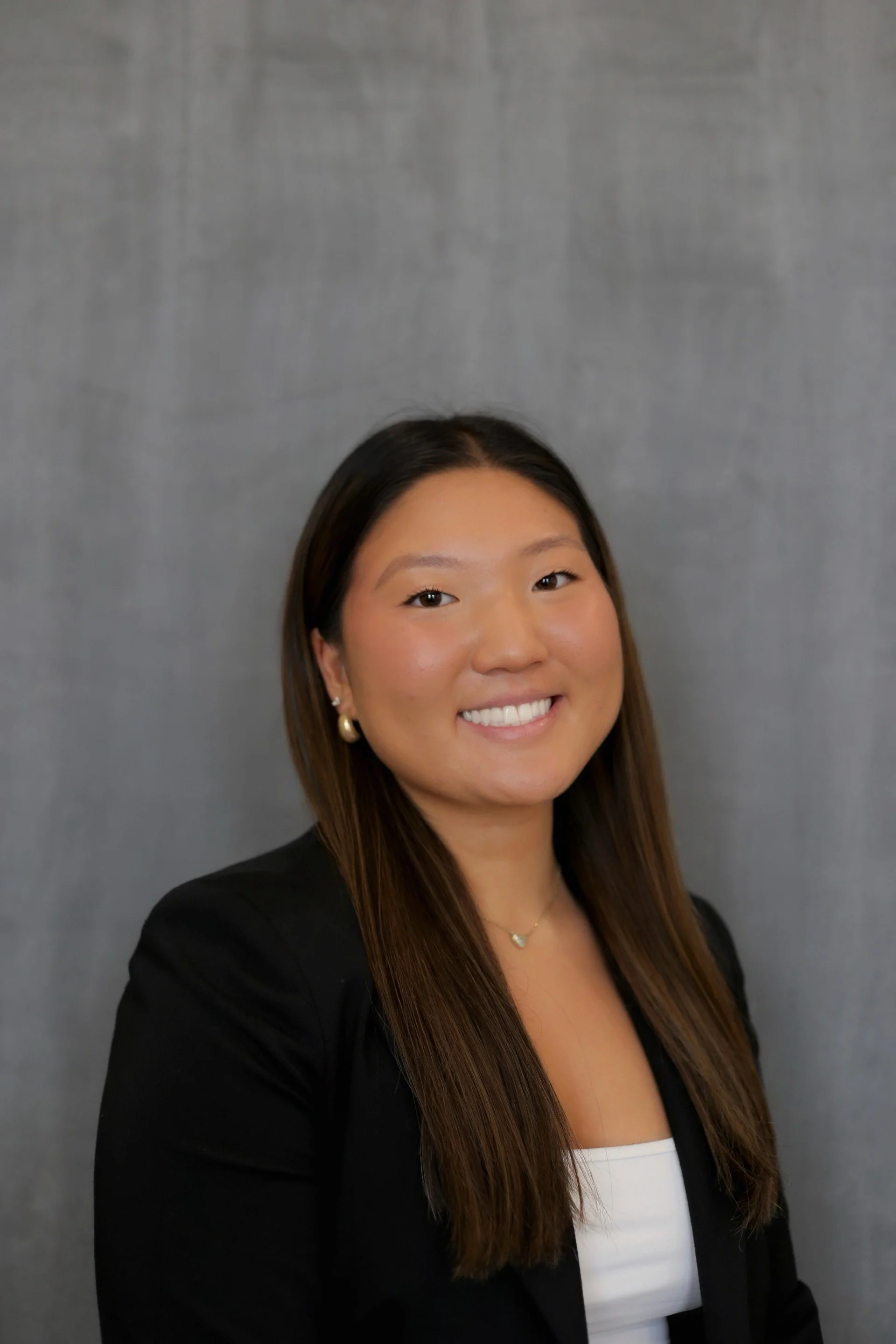 A young woman in professional attire smiling against a gray background.