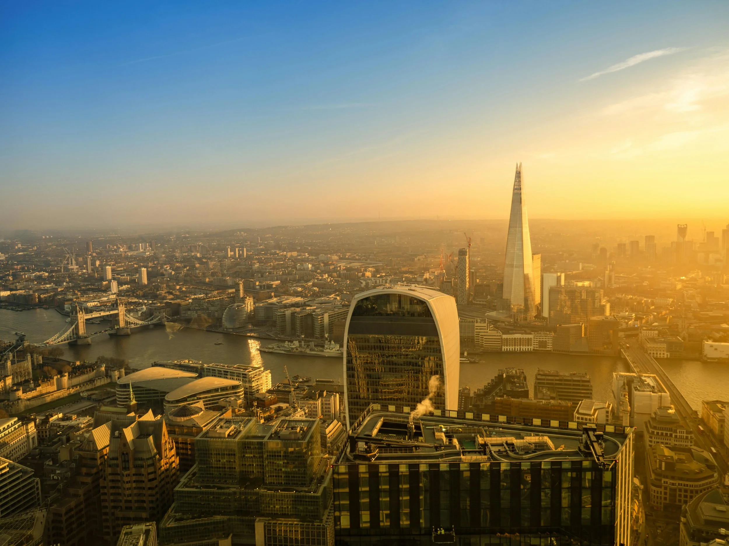 Sunset view of London skyline featuring the Shard, the Walkie Talkie building, Tower Bridge, and River Thames.
