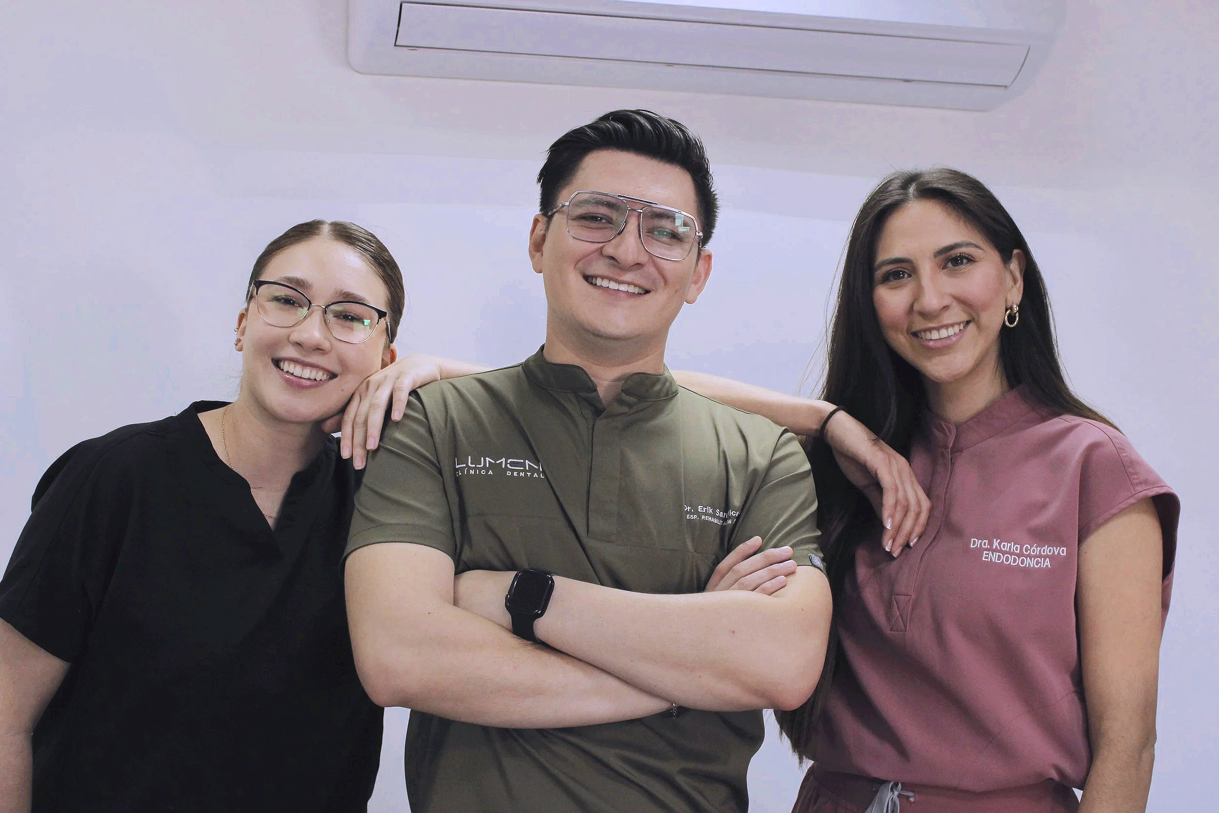 Tres profesionales de la salud, dos mujeres y un hombre, sonriendo y posando juntos en un consultorio dental, con un aire de confianza y amistad.