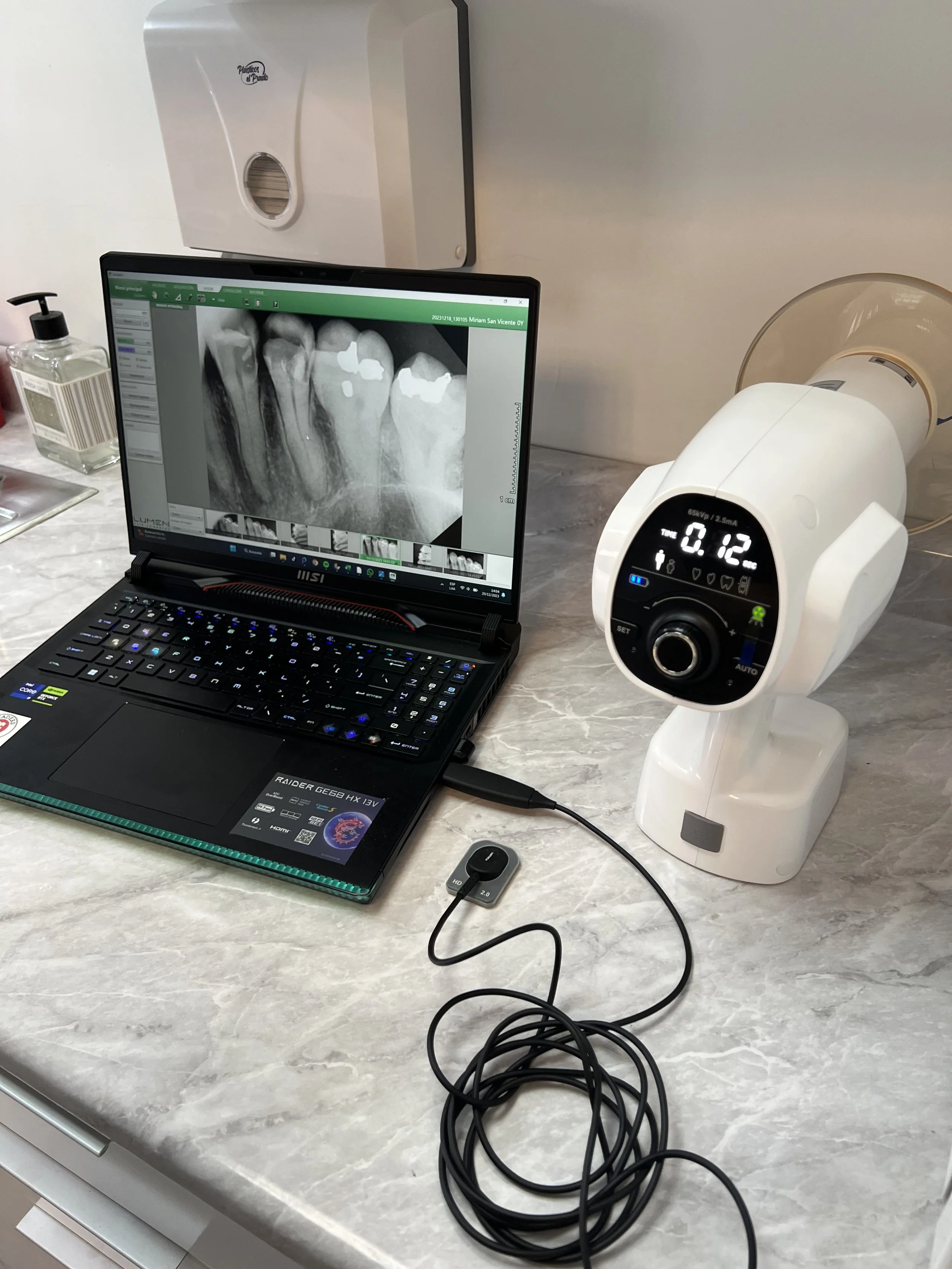 Monitor de radiografía dental, laptop y equipo de odontología en una mesa de clínica.