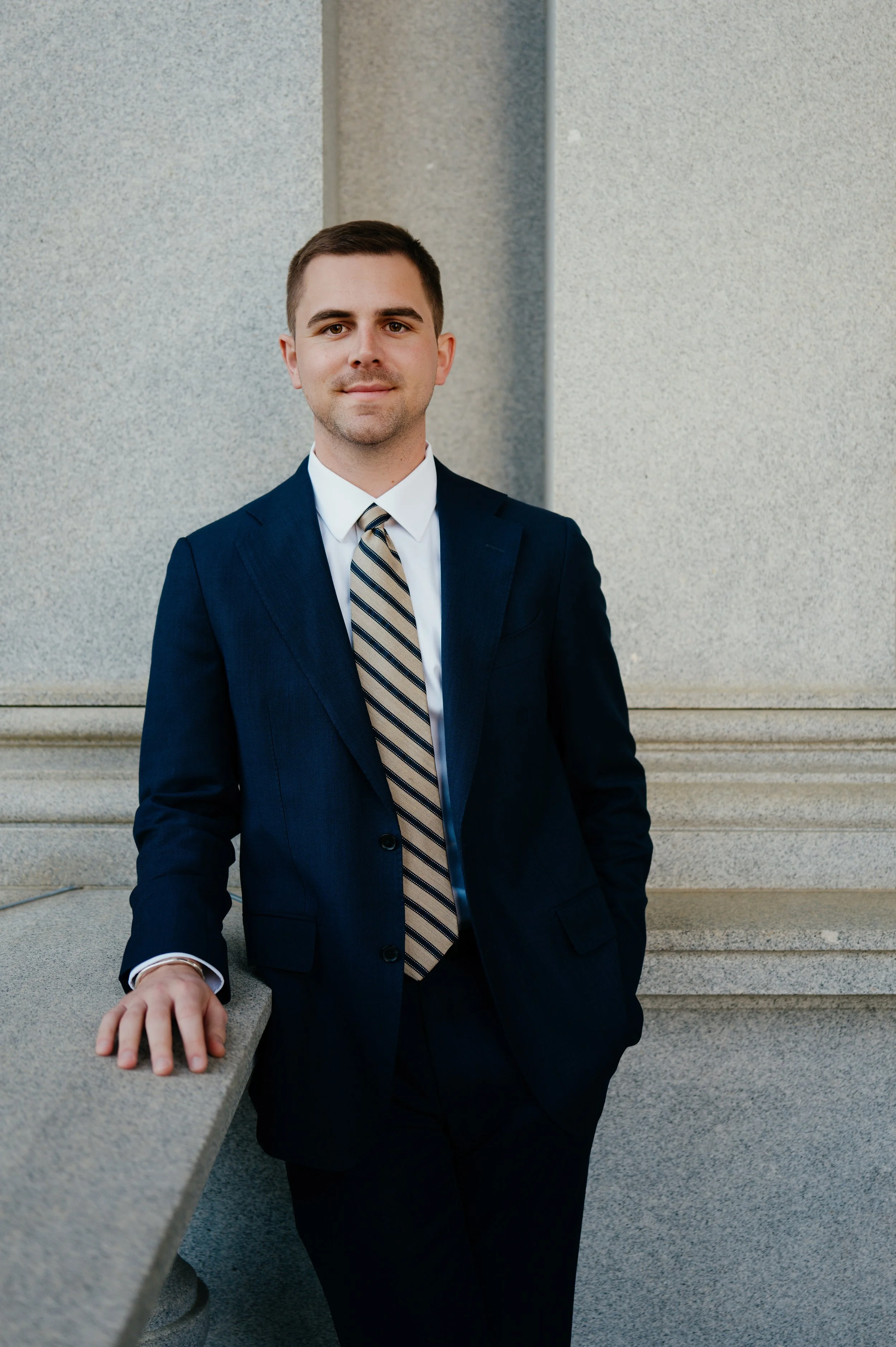 A man in a dark suit and striped tie standing outdoors against a concrete wall with stairs. White House Media booking, Conservative media booker, Eisenhower Executive Office Building