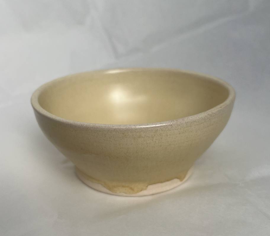 A cream-colored ceramic bowl with a slightly darker speckled exterior, placed on a light surface.