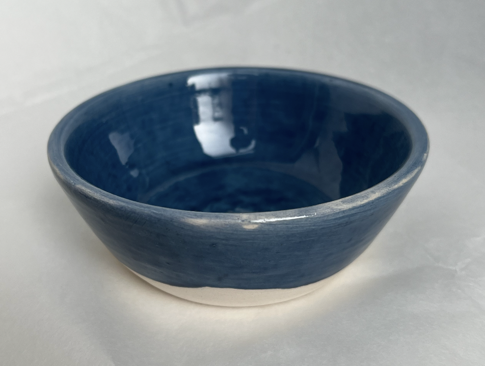 A ceramic bowl with a blue glaze on the inside and a white unglazed base, placed on a plain white surface.