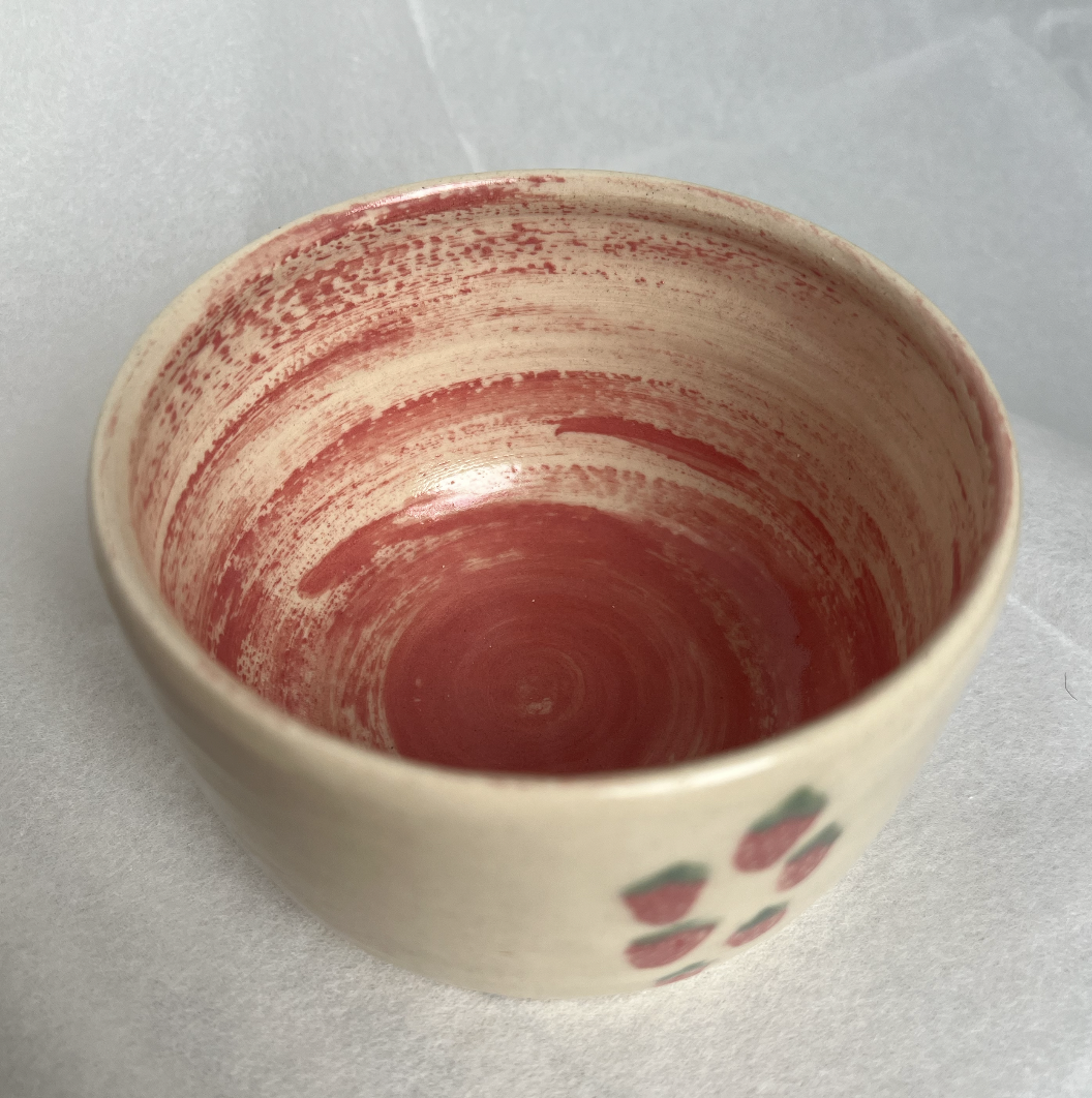 A ceramic bowl with a red and white swirl pattern inside, and small strawberry designs on the exterior.
