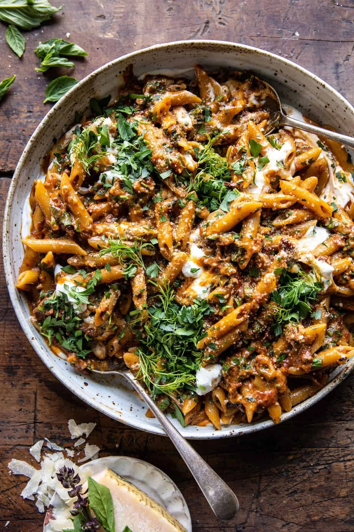 A bowl of cooked pasta with tomato-based sauce, fresh herbs, and cheese on a wooden table.