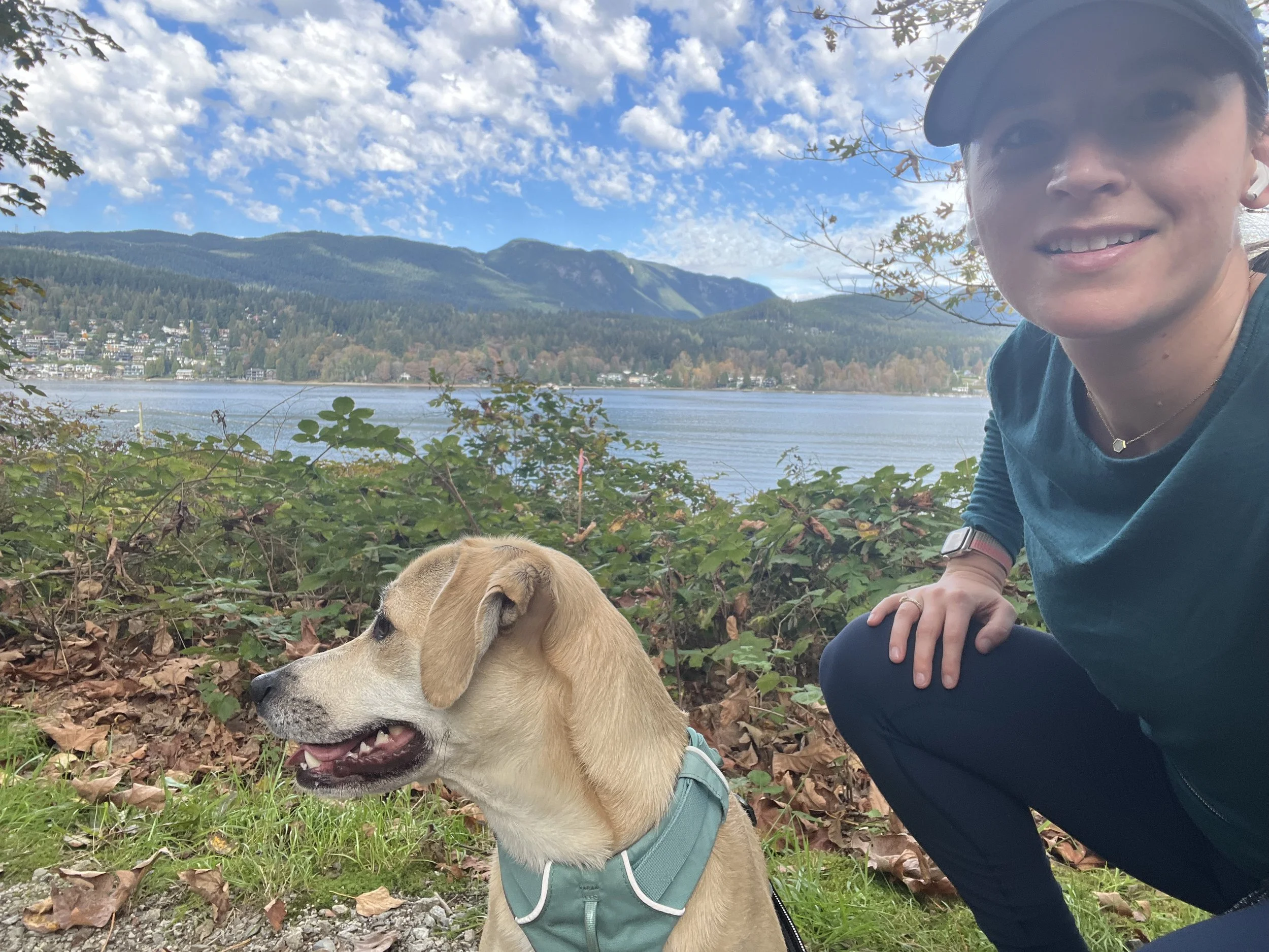 Sophia crouching with her dog Emmy with a blue sky and scattered cloud backdrop
