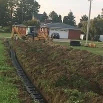 A backyard with a garden bed being prepared, a tractor parked, and a shed and trees in the background.