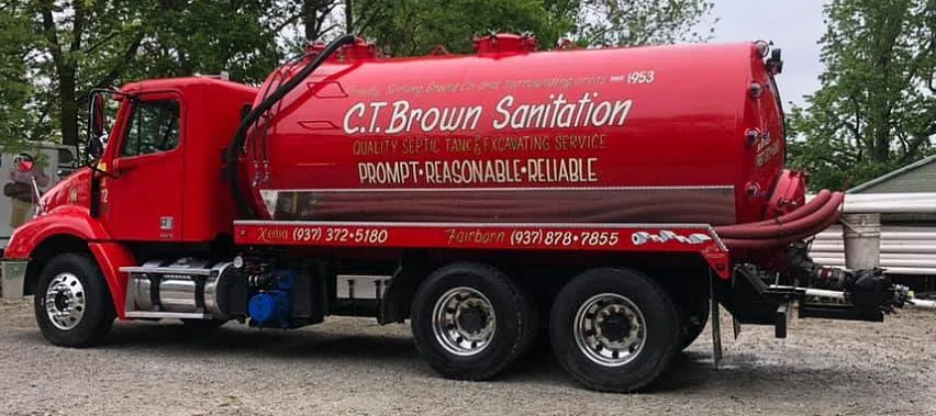 Red sanitation truck with the company name 'C.T. Brown Sanitation' and contact information, parked on a gravel surface with trees in the background.