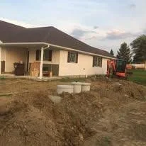 A house under construction with a dirt yard and construction equipment nearby.