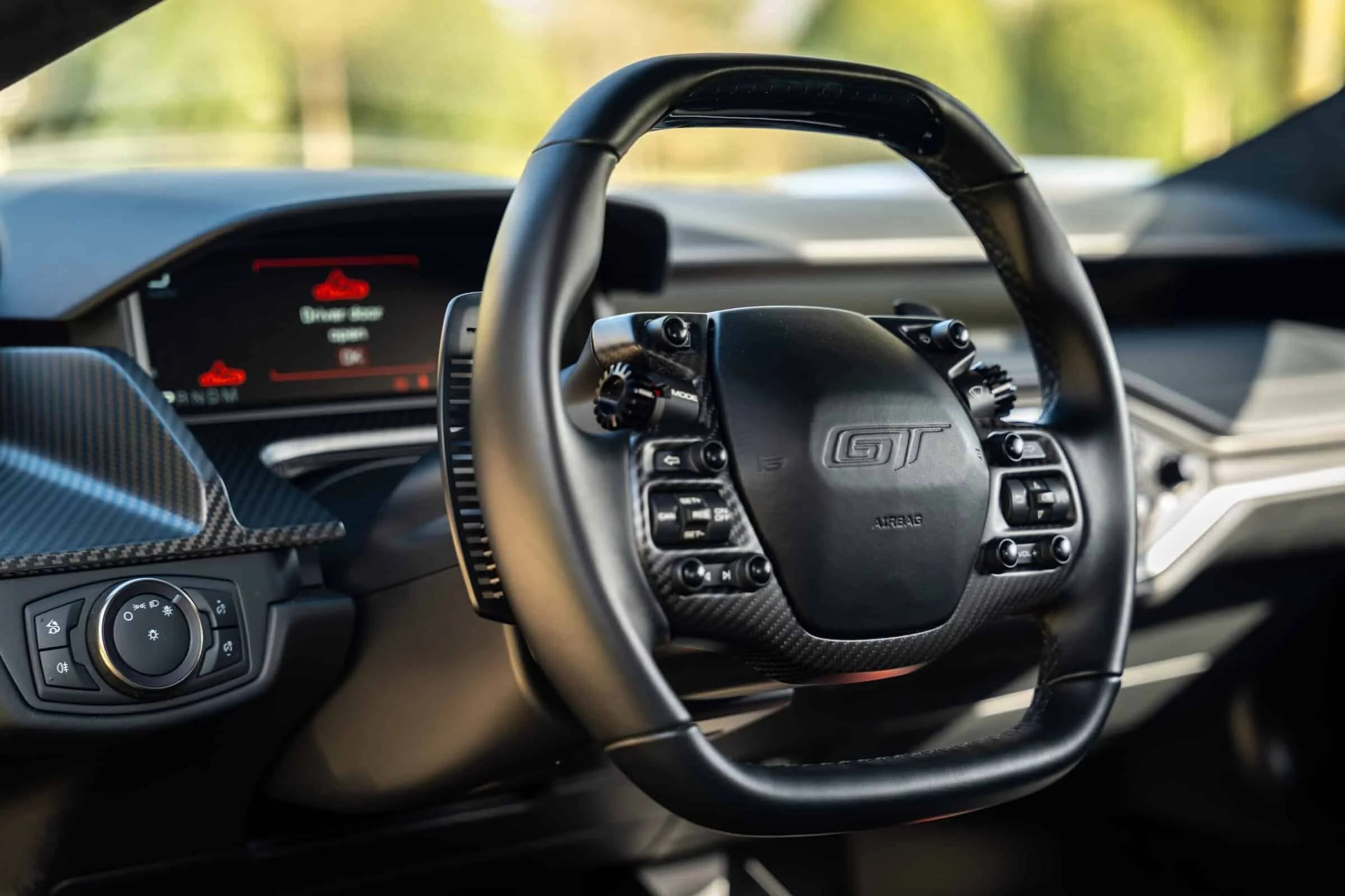 Close-up view of a sporty Porsche GT steering wheel inside a car's interior with an electronic display in the background.