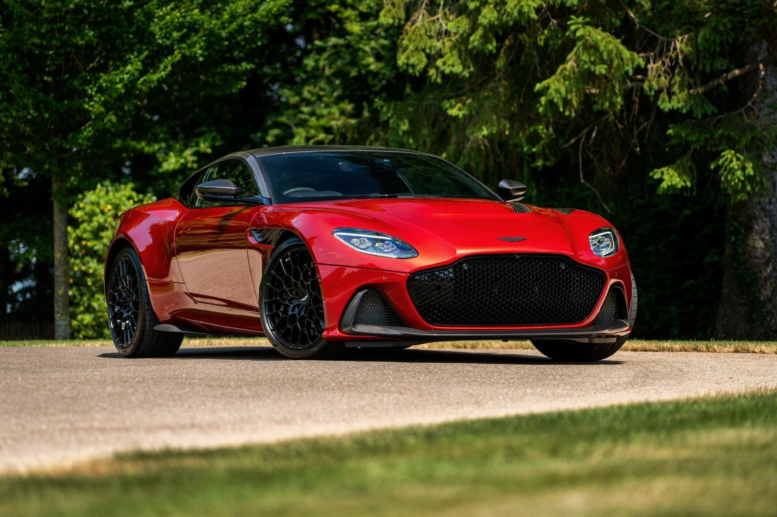 Red sports car parked on a driveway with green trees in the background.