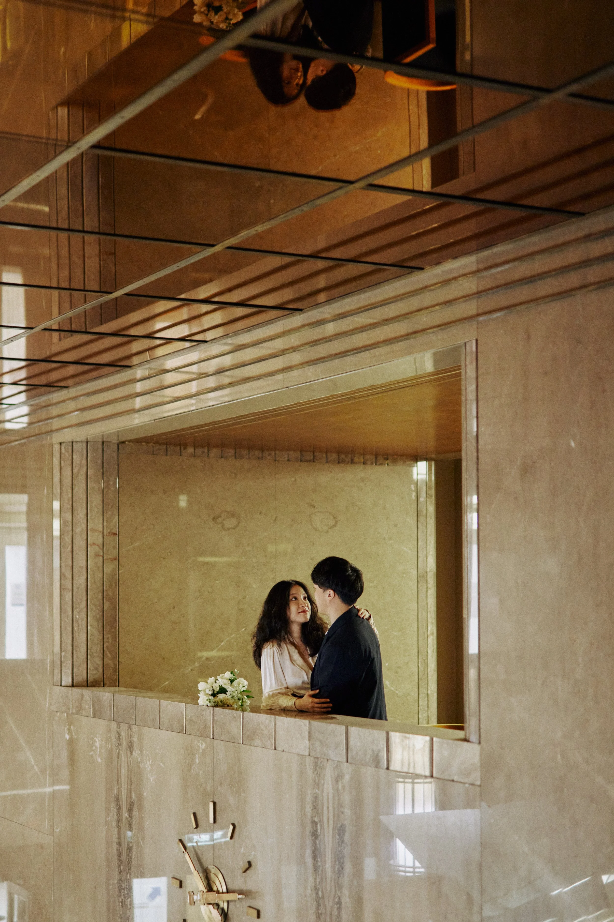 A couple is dancing in an elegant lobby or reception area, with the woman holding a bouquet of flowers, and they are looking at each other lovingly.