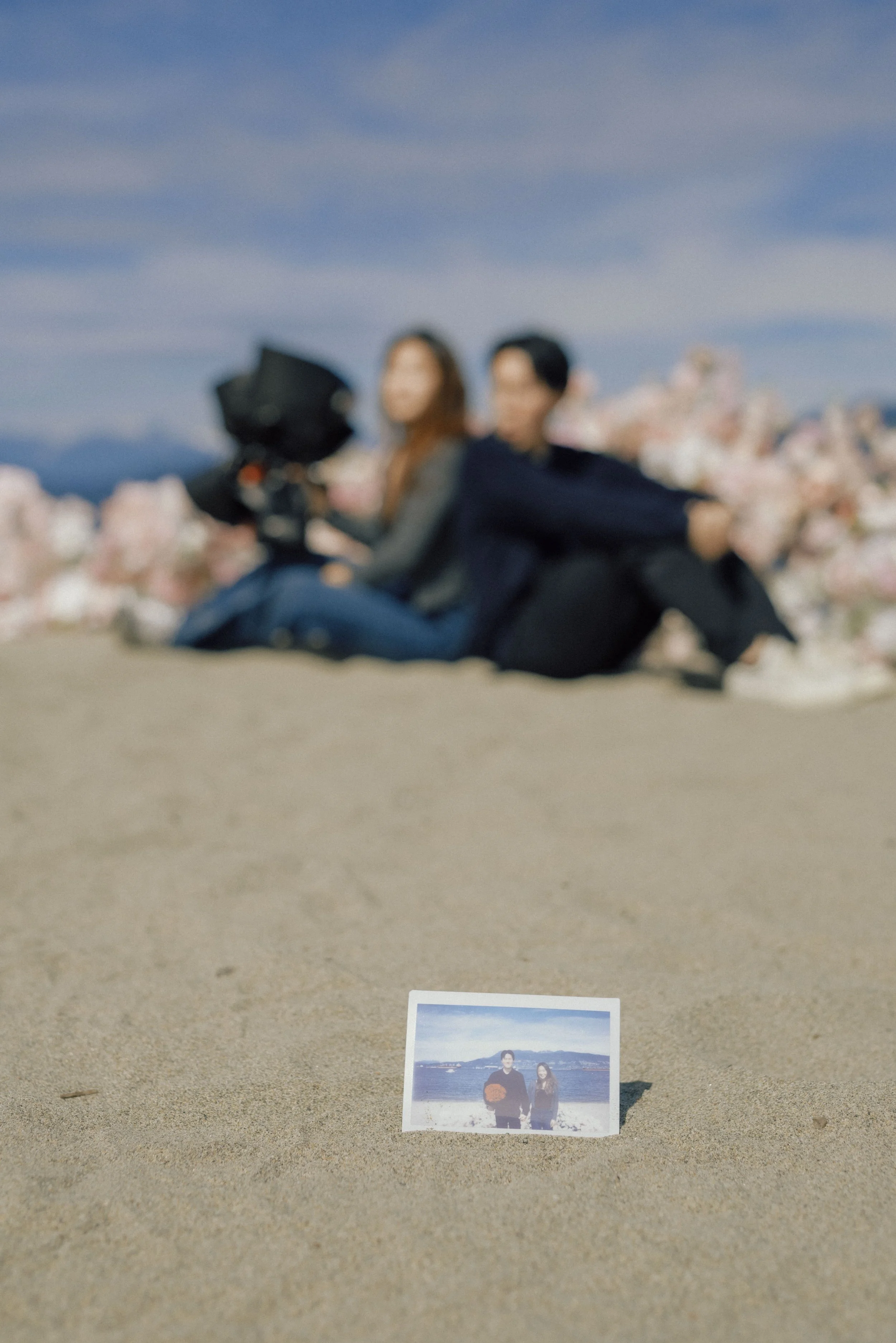 A blurry photograph of two people on a sandy beach with a framed picture of the same two people in the foreground, near the sand, with a mountain and ocean in the background.